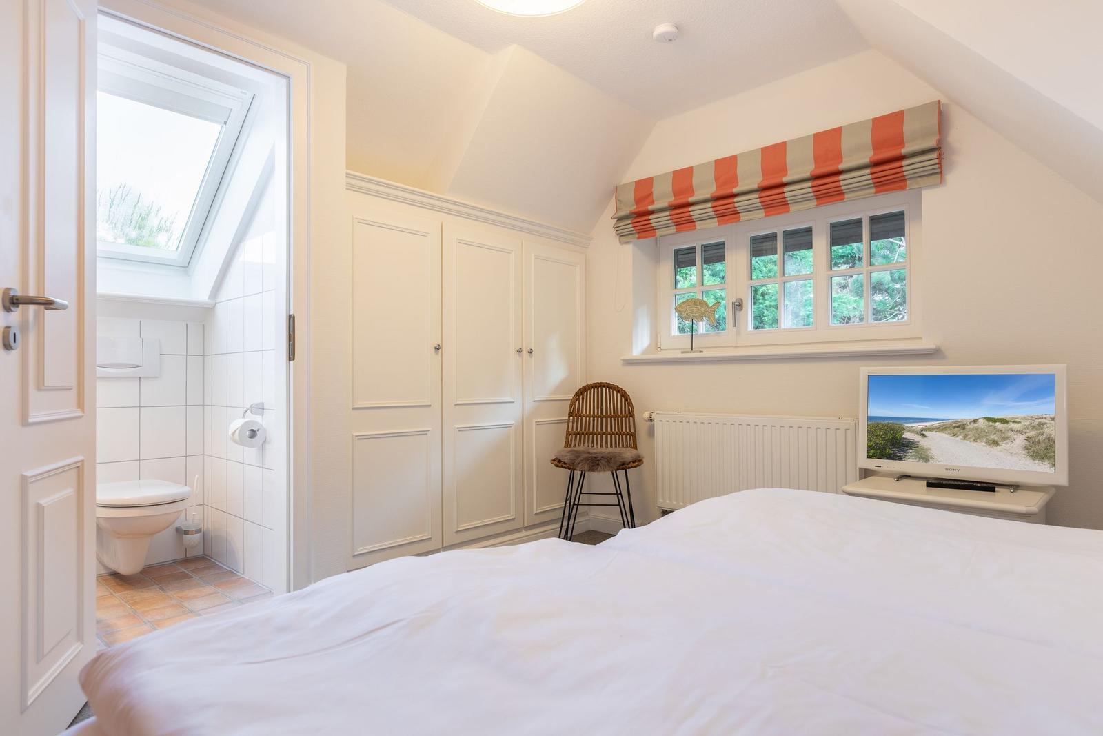 Bedroom with sloped ceiling, window, TV, and adjacent toilet.