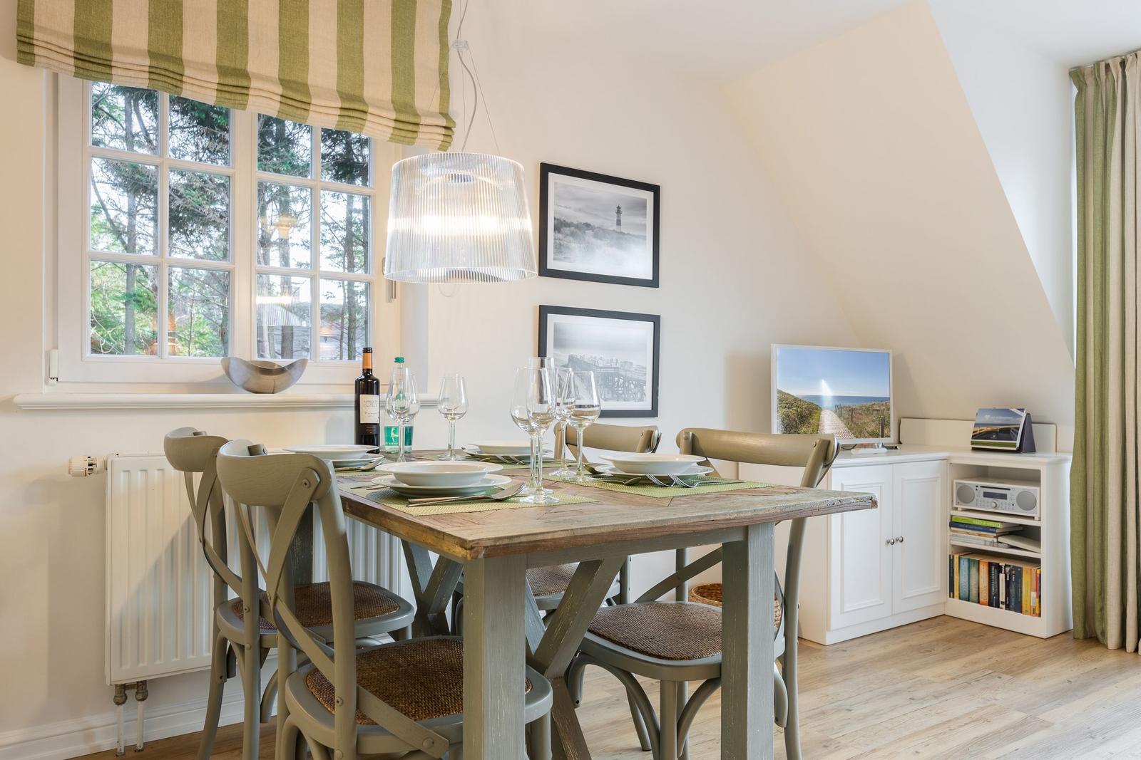 Dining room with wooden table, chairs, and window overlooking trees.