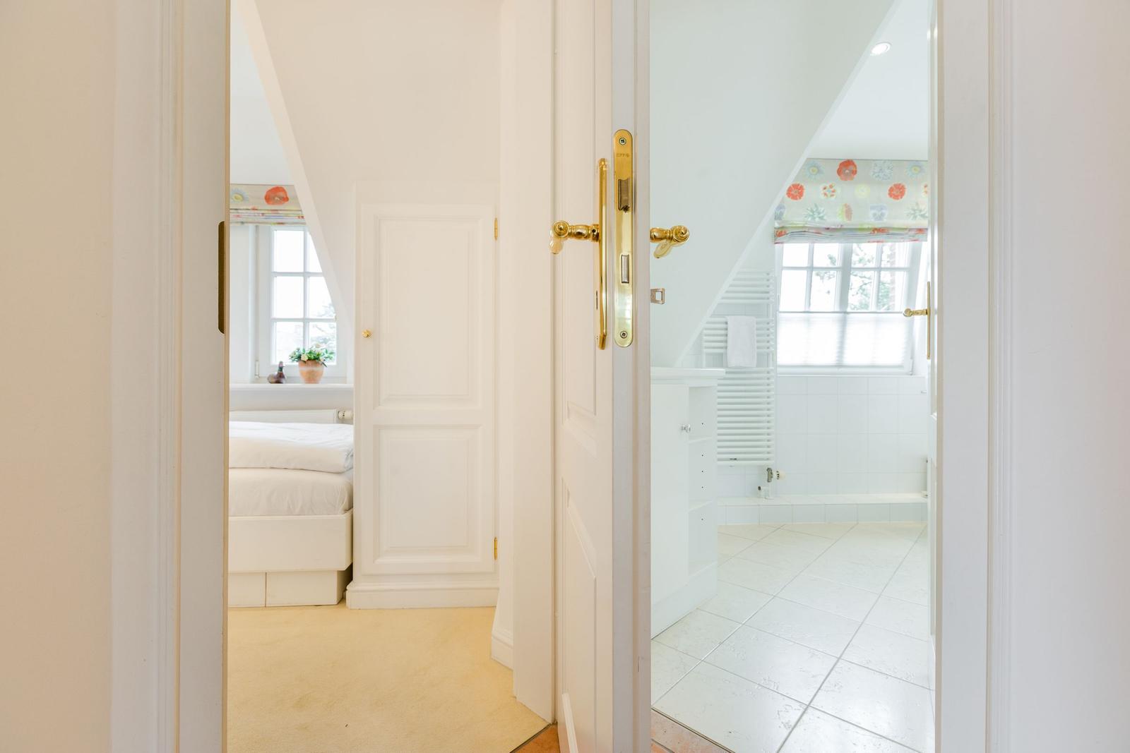 Bedroom and bathroom with sloped ceilings and white walls.