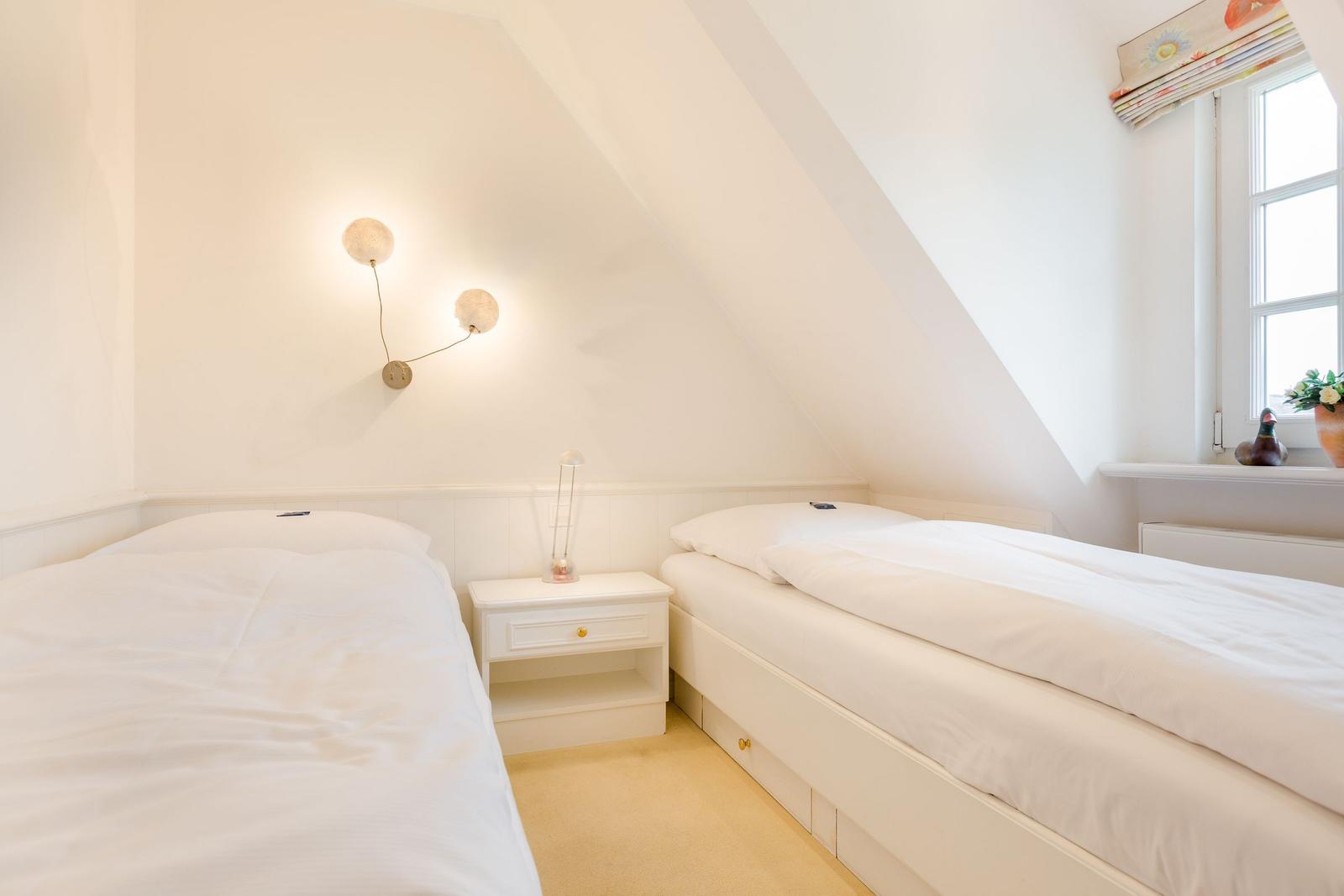 Two beds in an attic room with window and nightstand.