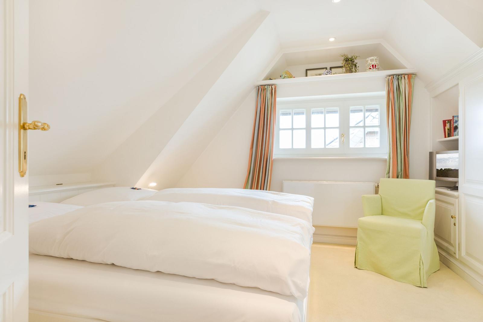 Double bedroom with sloped ceiling, window, and green seating.