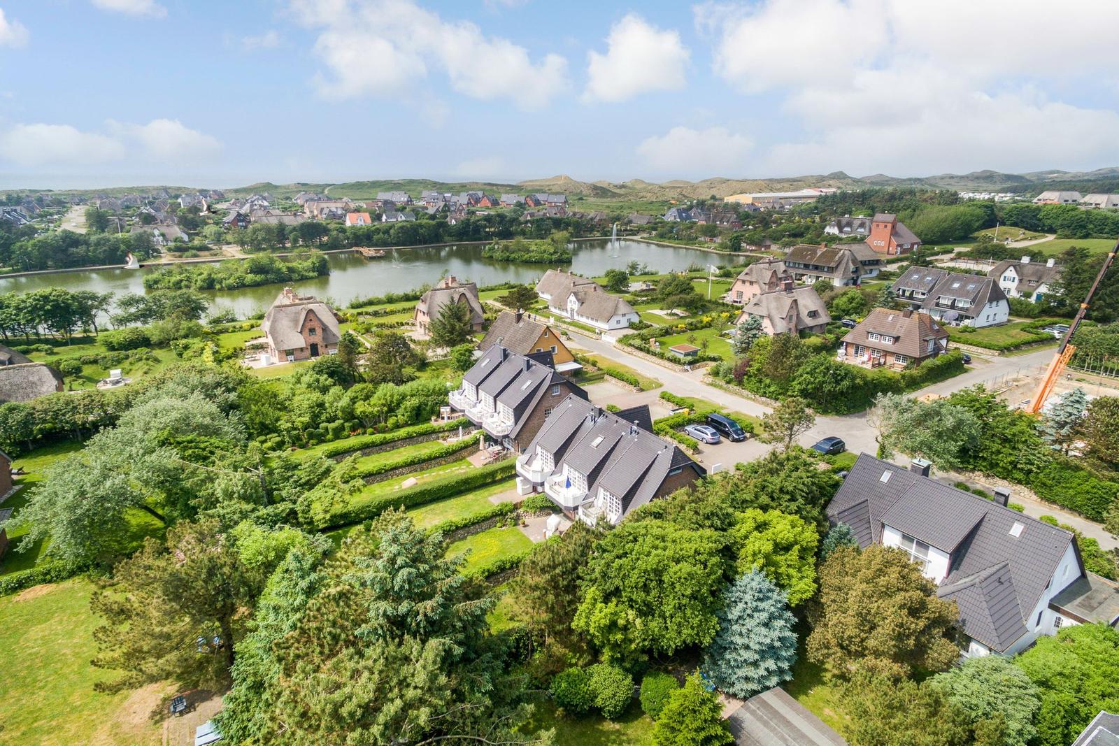 Aerial view of houses around a lake with green areas and hills in the background.