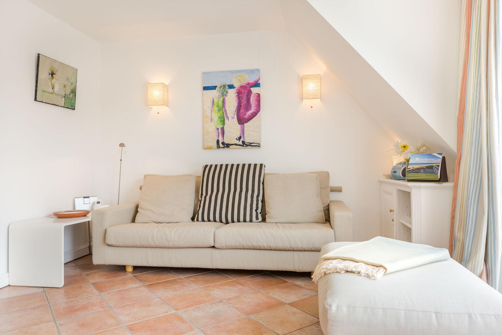 Living room with sofa, wall art, and terracotta floor under sloped ceiling.
