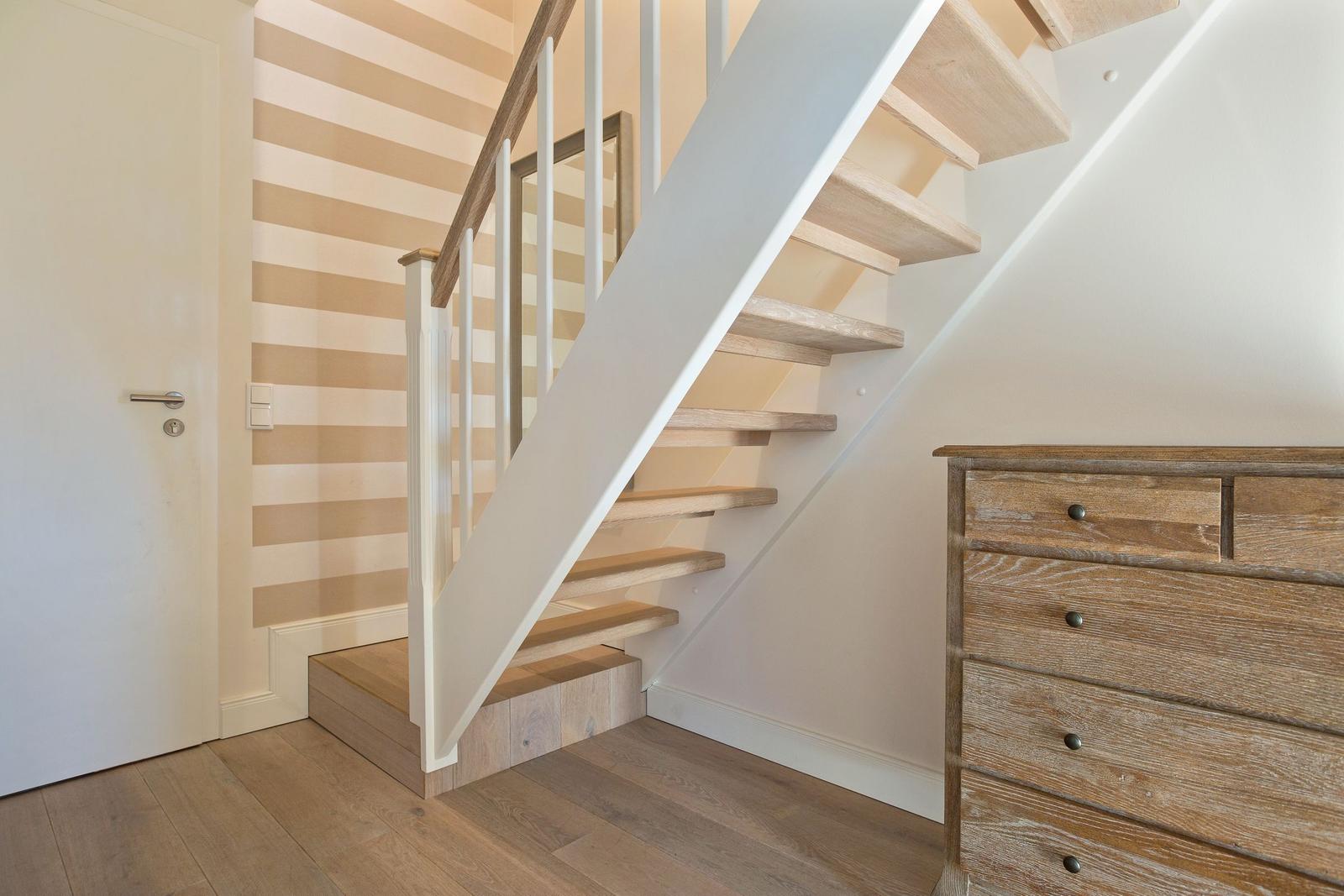 Staircase with wooden steps, white balustrade, and striped wall