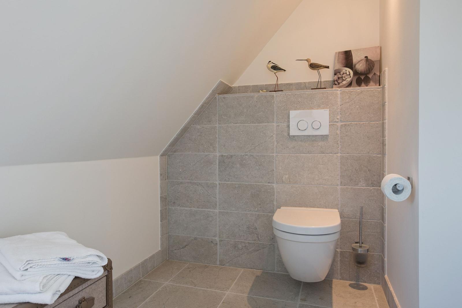 Bathroom with toilet, gray tiles, and decorative birds on the wall.