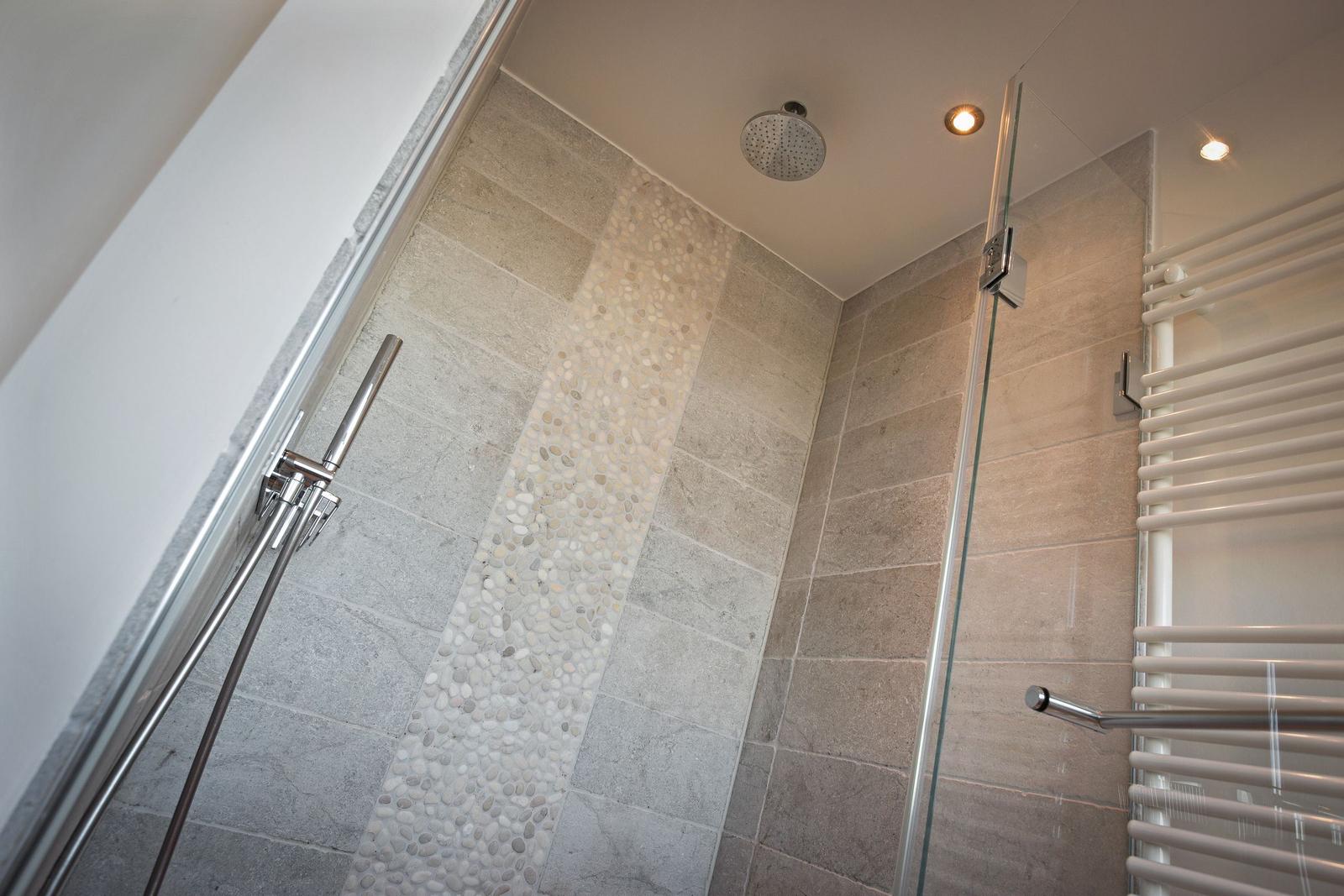 Shower area with glass wall, stone tiles, and shower head on the ceiling.
