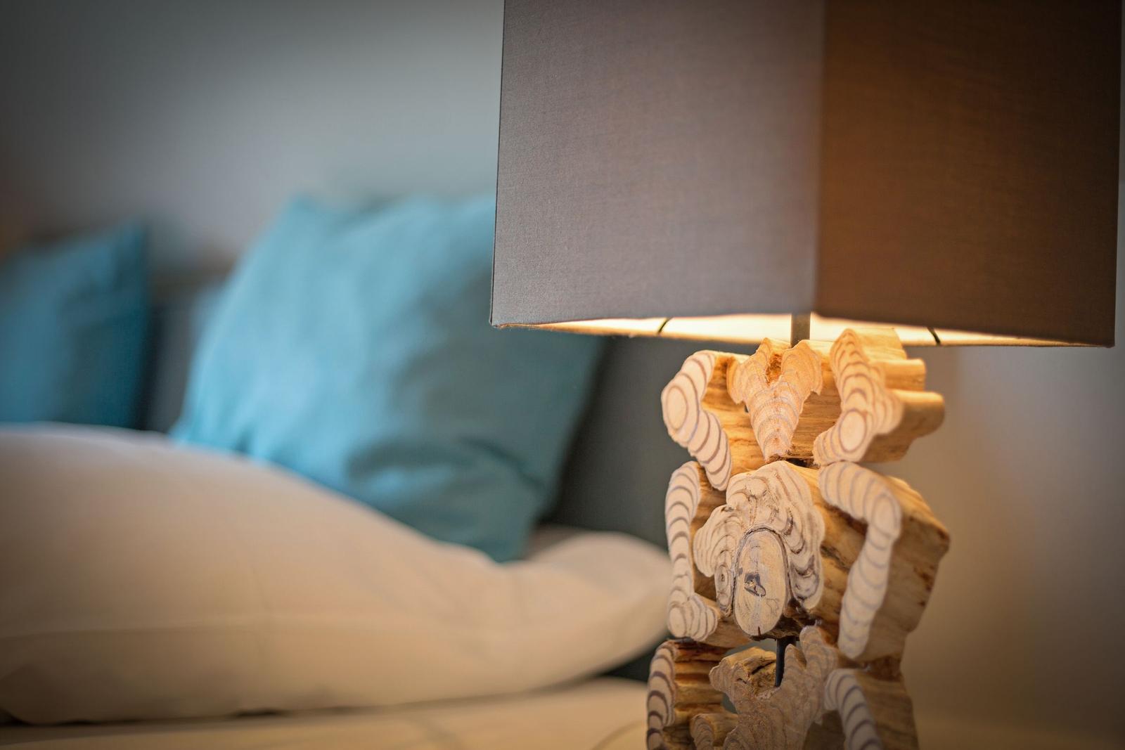 Nightstand lamp with wooden figure beside bed with pillows.