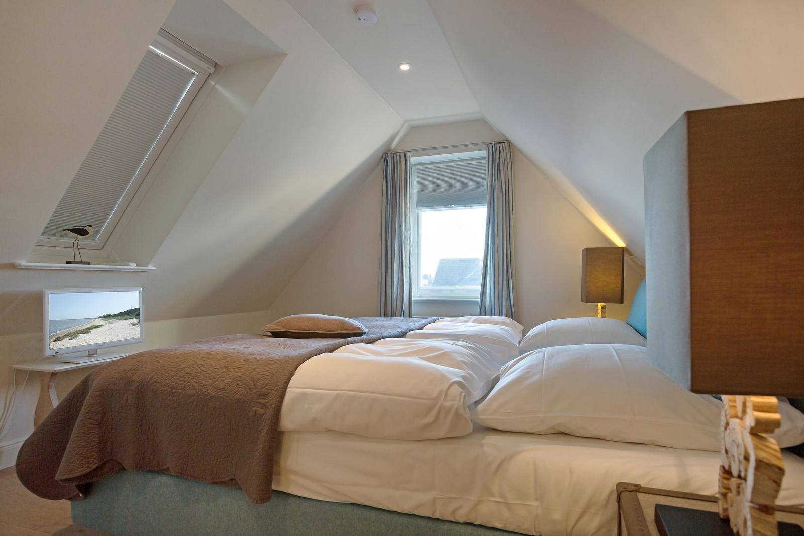 Bedroom with sloped ceiling, bed, window, and TV.