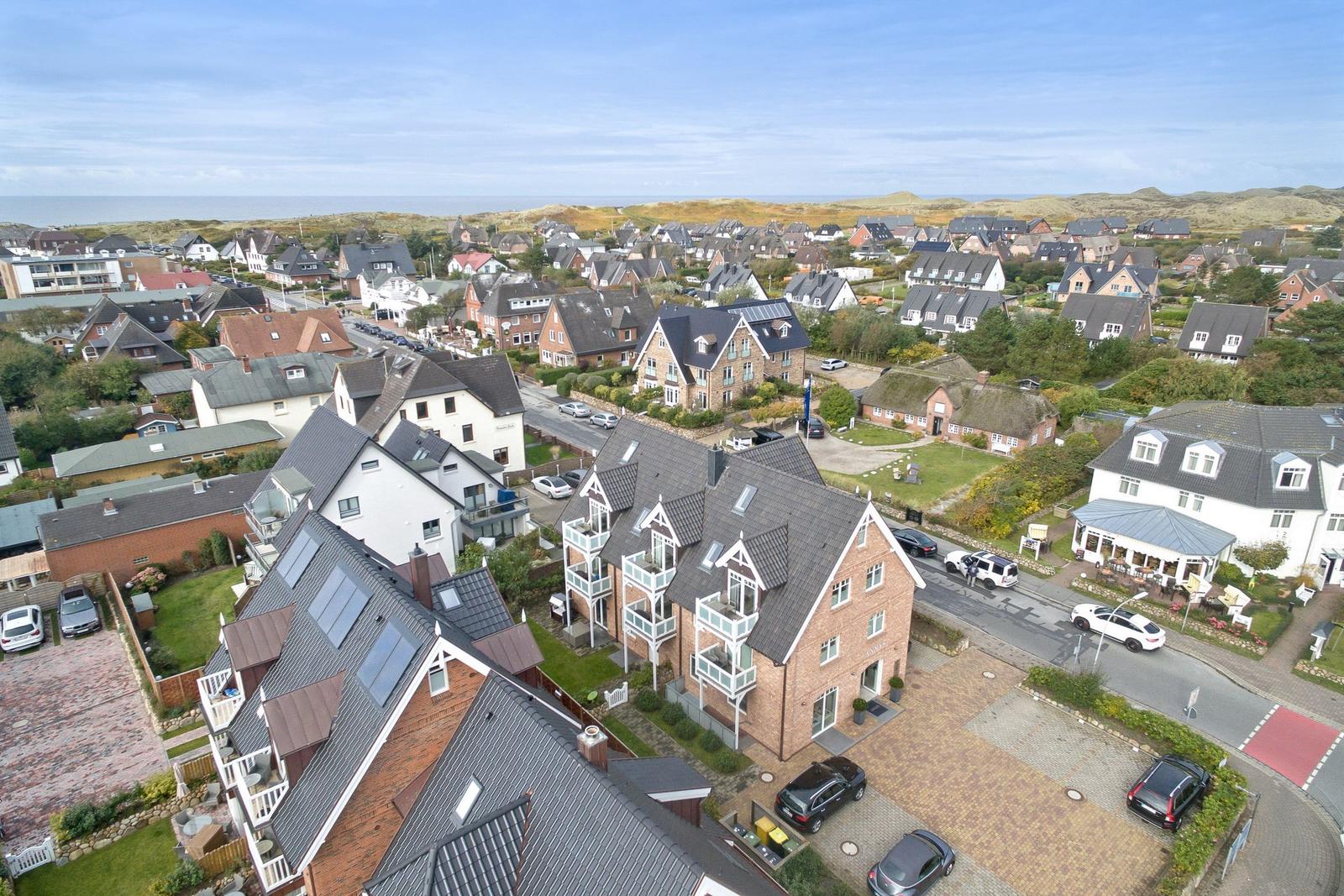 Aerial view of a residential area near the sea with houses and parked cars.