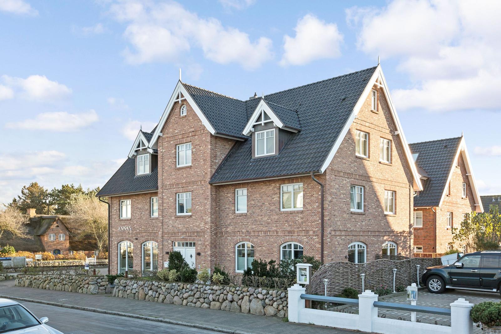 Brick house with dark roof and white window frames. Forecourt with stone wall and paved area.