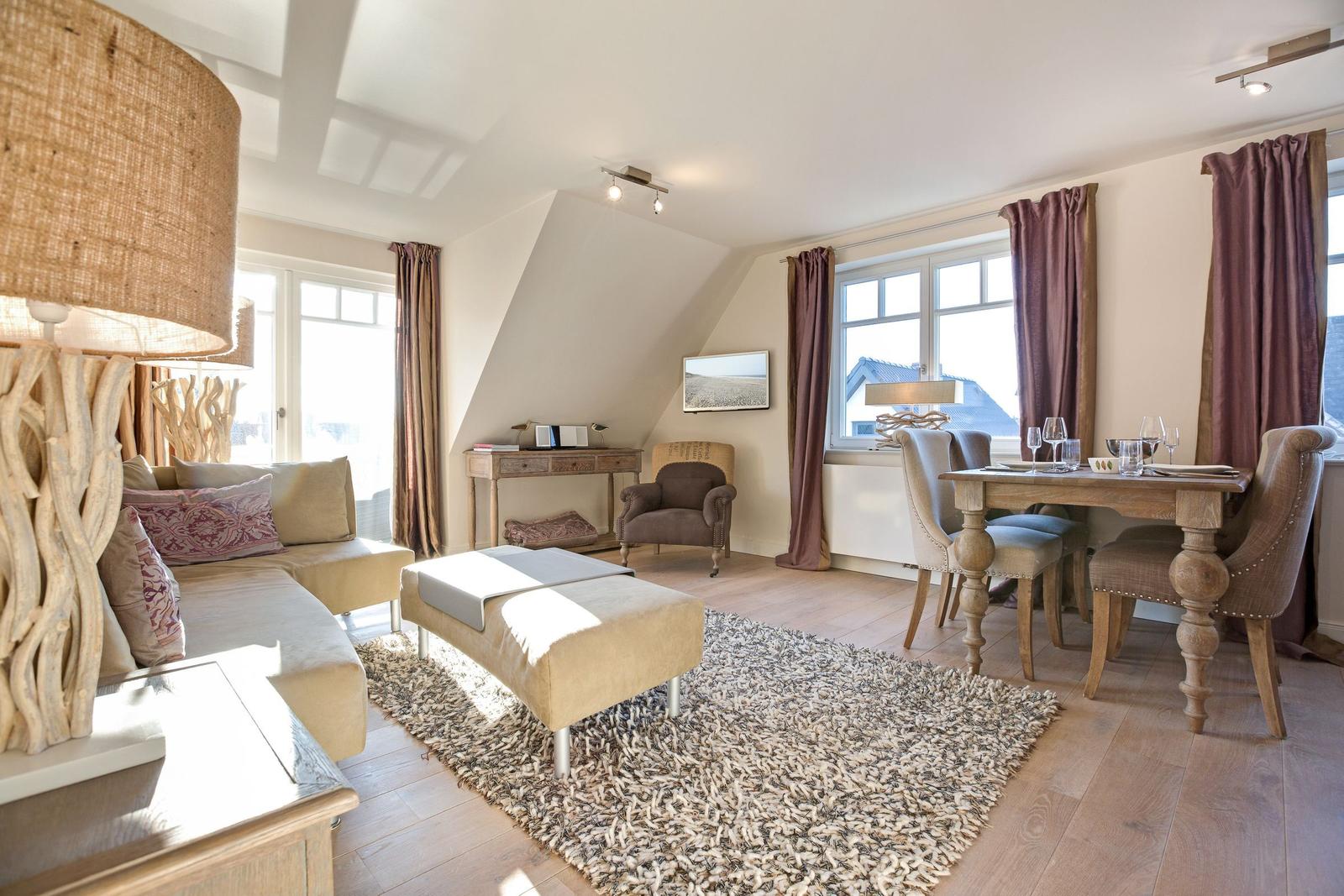 Living and dining area with sofa, table and chairs. Wooden floor and large windows.