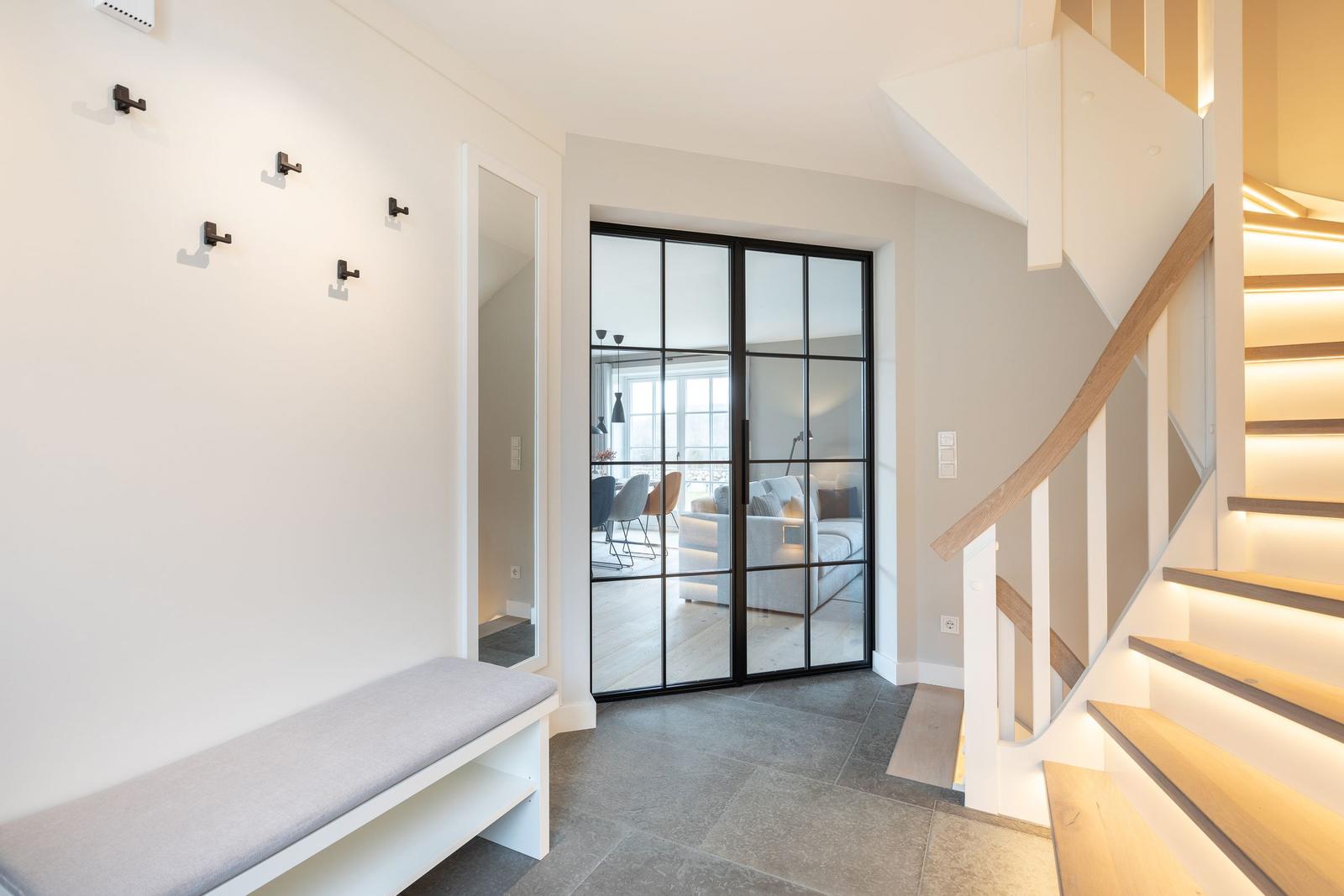Eingang mit Bank, Garderobe und Blick in Wohnbereich über Glaswand.