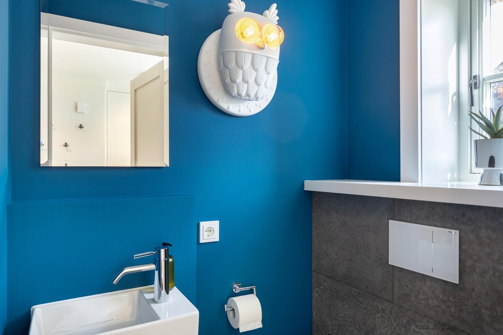 Badezimmer mit blauen Wänden, Spiegel, Waschbecken und Eule-Lampe.