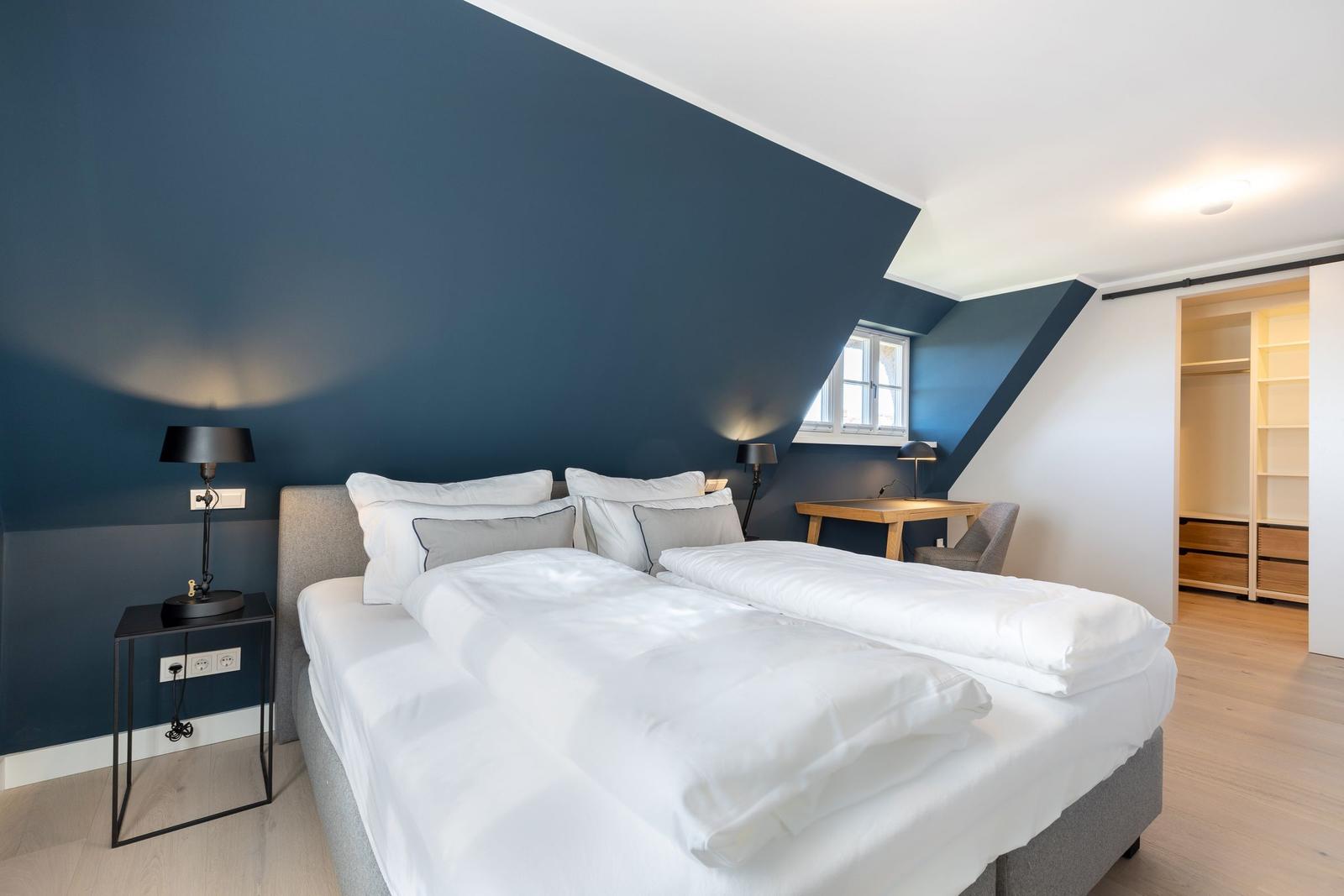 Schlafzimmer mit Doppelbett, blauer Wand und Schreibtisch