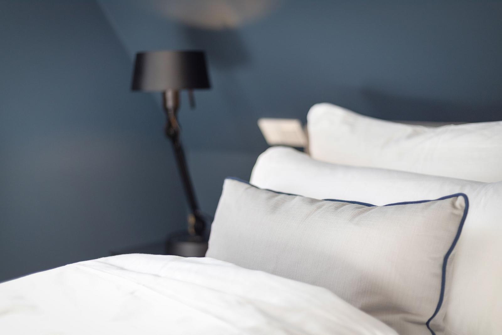 Bettkopfteil mit Kissen und Nachttischlampe vor blauer Wand