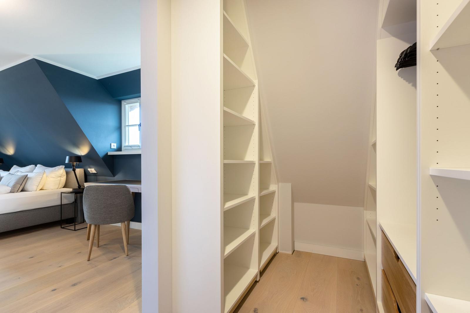 Schlafzimmer mit blauer Wand und Schrankbereich mit weißen Regalen.