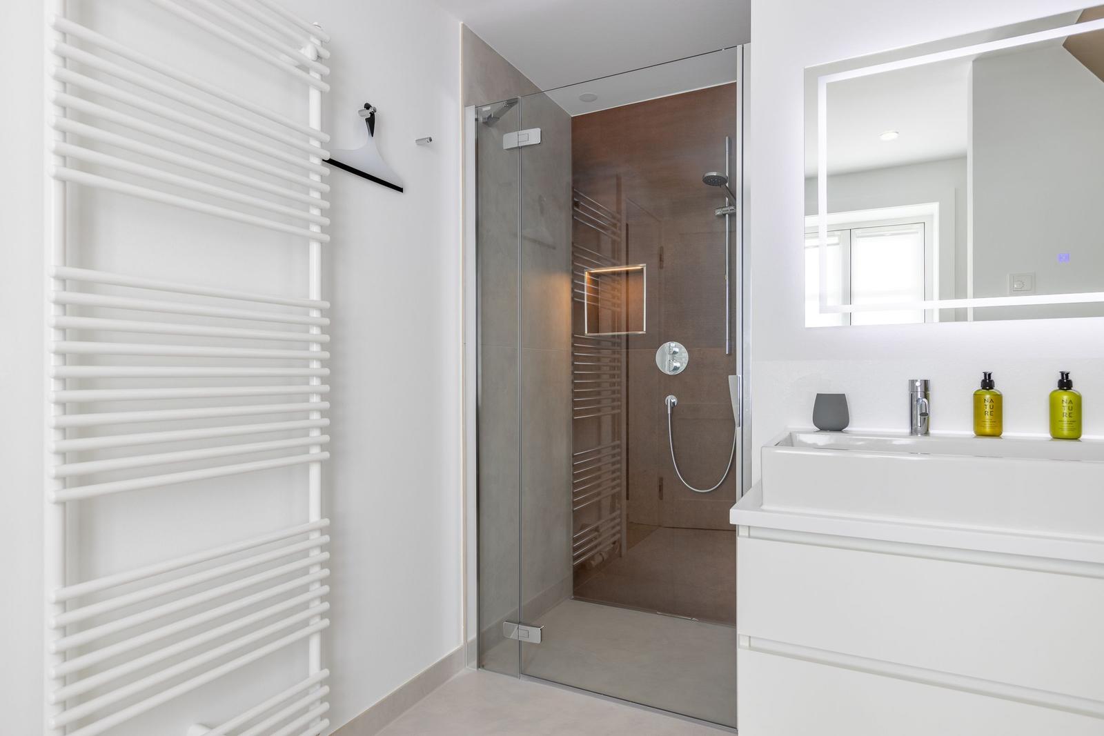 Dusche mit Glaswand, Waschbecken und Heizung.