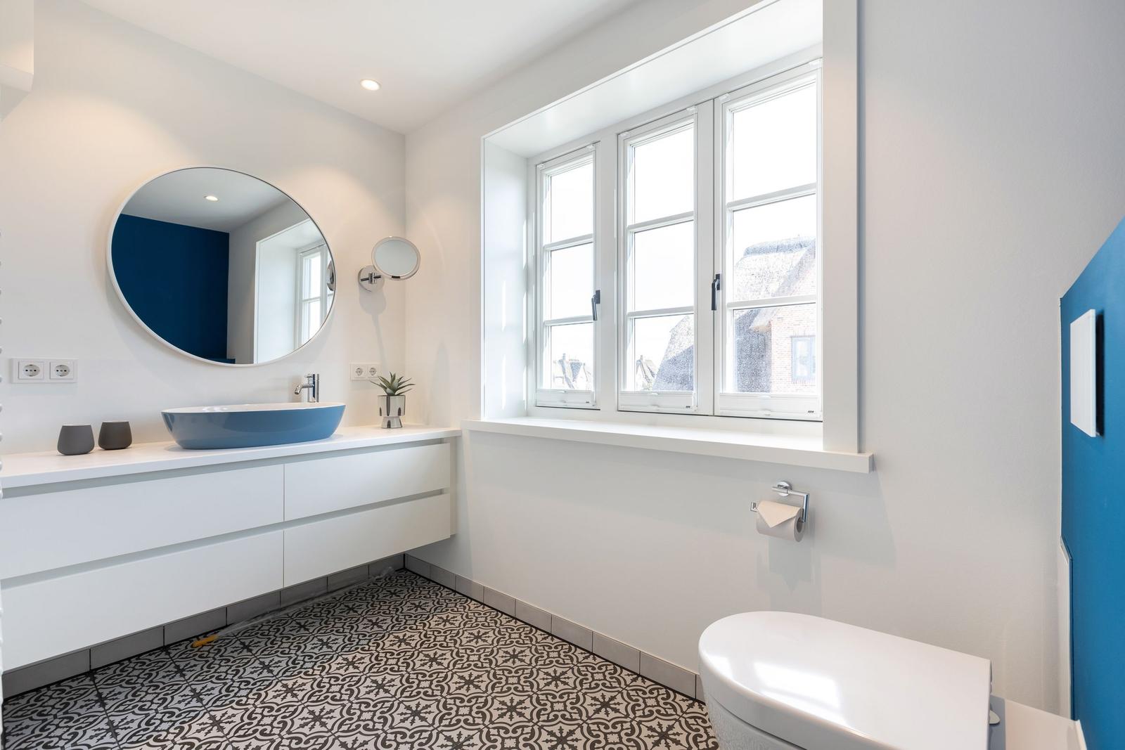 Badezimmer mit blauem Waschbecken, runden Spiegel und Fenster
