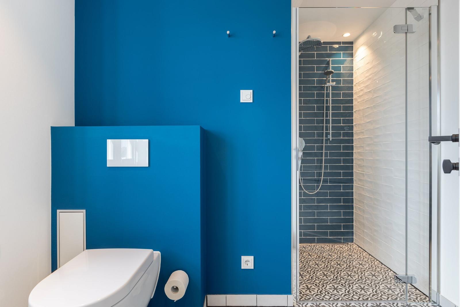 Badezimmer mit blauer Wand, Toilette und Dusche mit Glaswand.