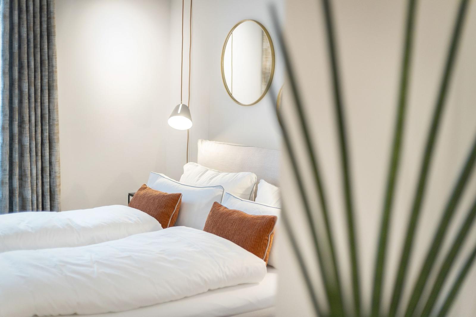 Schlafzimmer mit Bett, Kissen, Spiegel und Lampe.