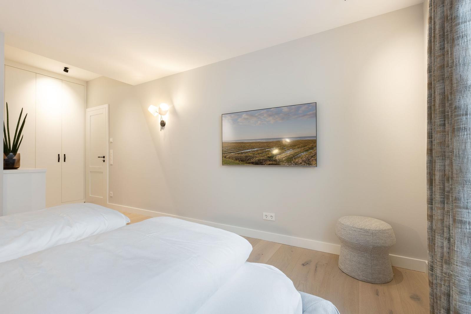Schlafzimmer mit zwei Betten, Wandbild und Stuhl.