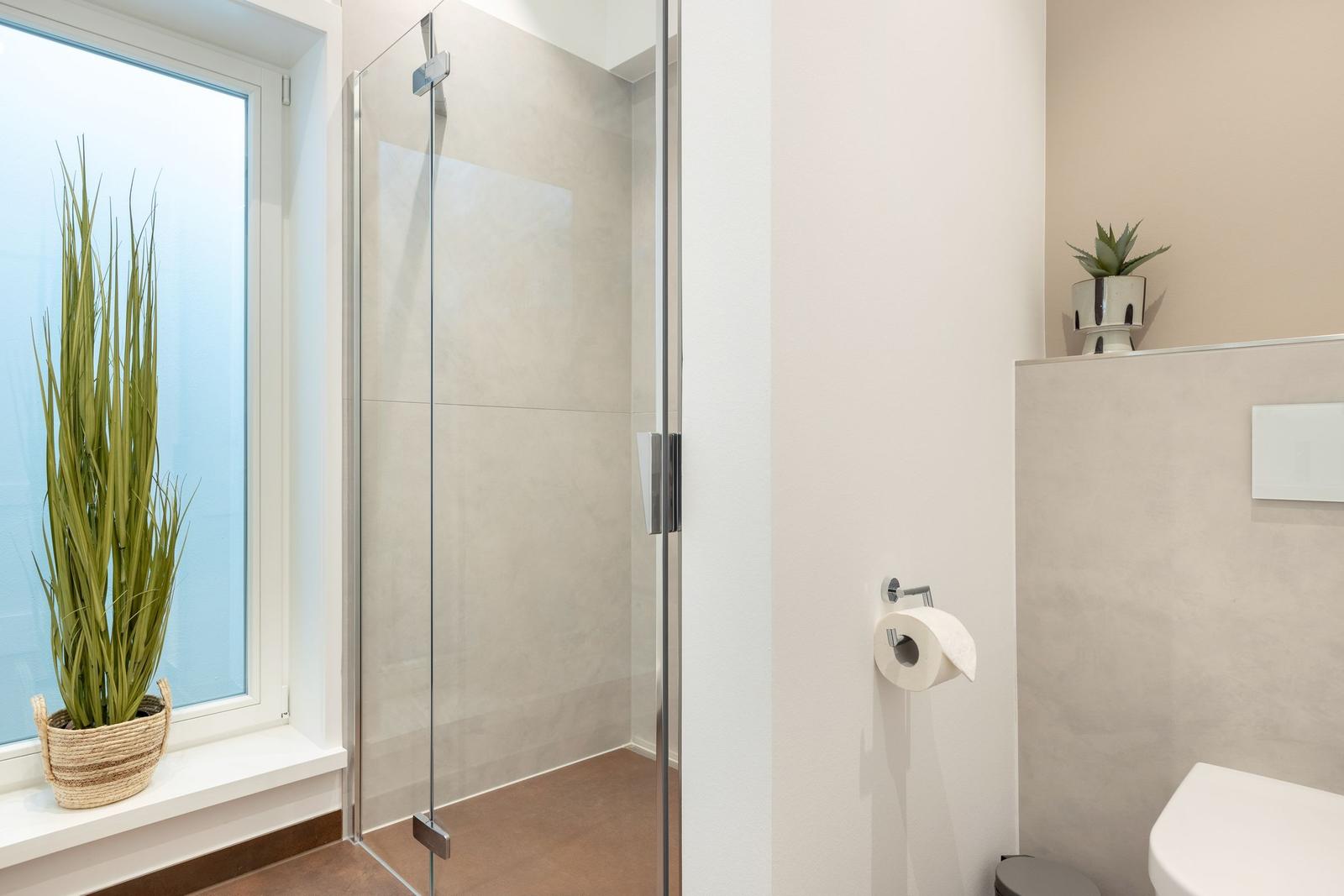 Badezimmer mit Dusche, Toilette und Pflanzen an Fensterbank.