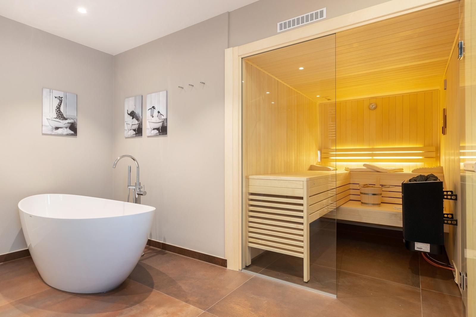 Bad mit freistehender Badewanne und Sauna im Hintergrund.