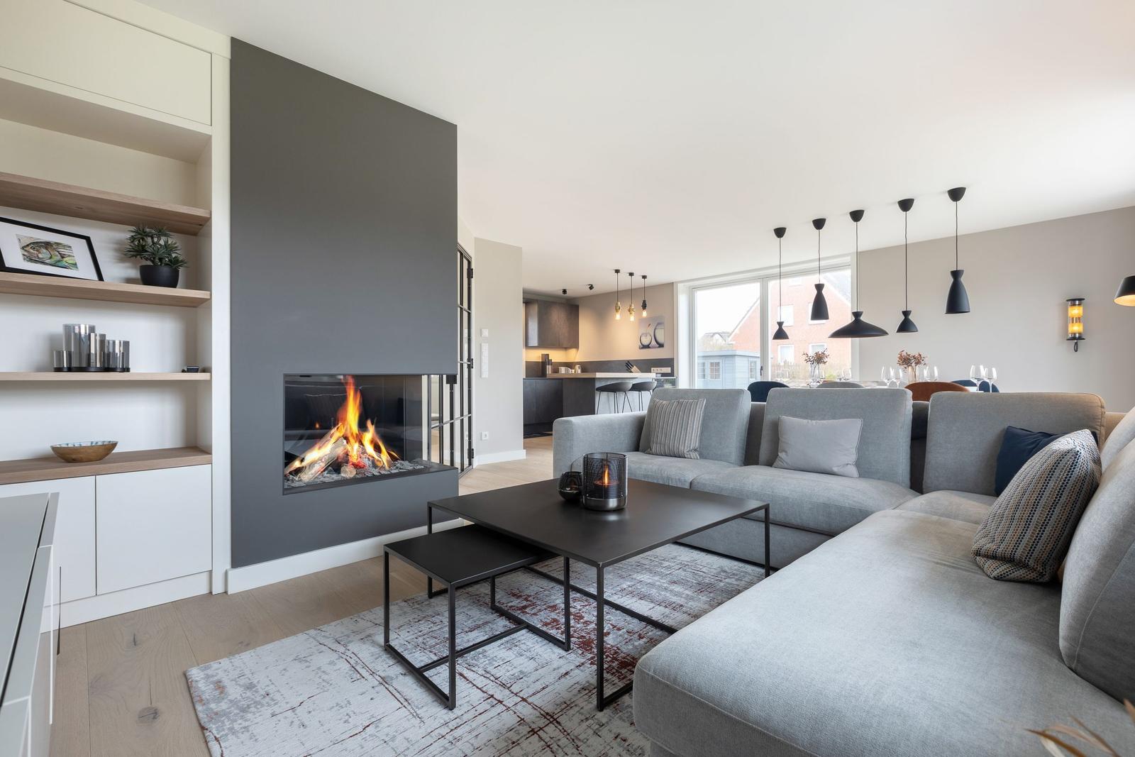 Wohnzimmer mit Kamin, Sofa und Esstisch. Moderne Einrichtung mit schwarzen Lampen.