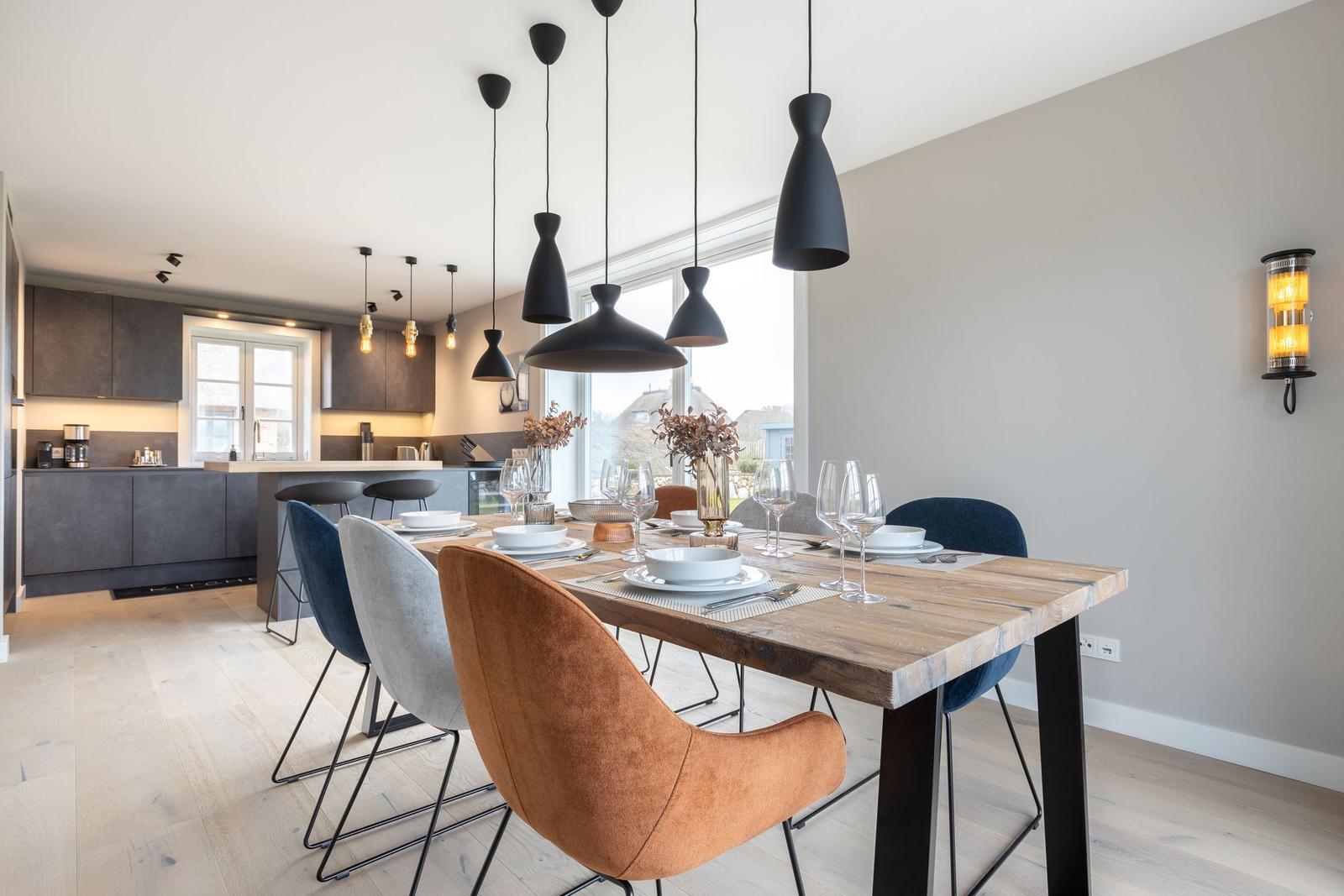 Essbereich mit Holztisch und Stühlen, Küchenbereich im Hintergrund, moderne Pendelleuchten.