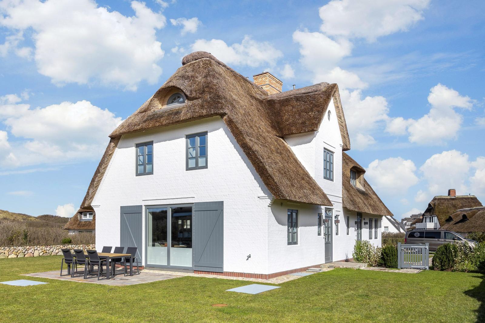 Ein weißes Haus mit Strohdach und Terrasse im Freien.