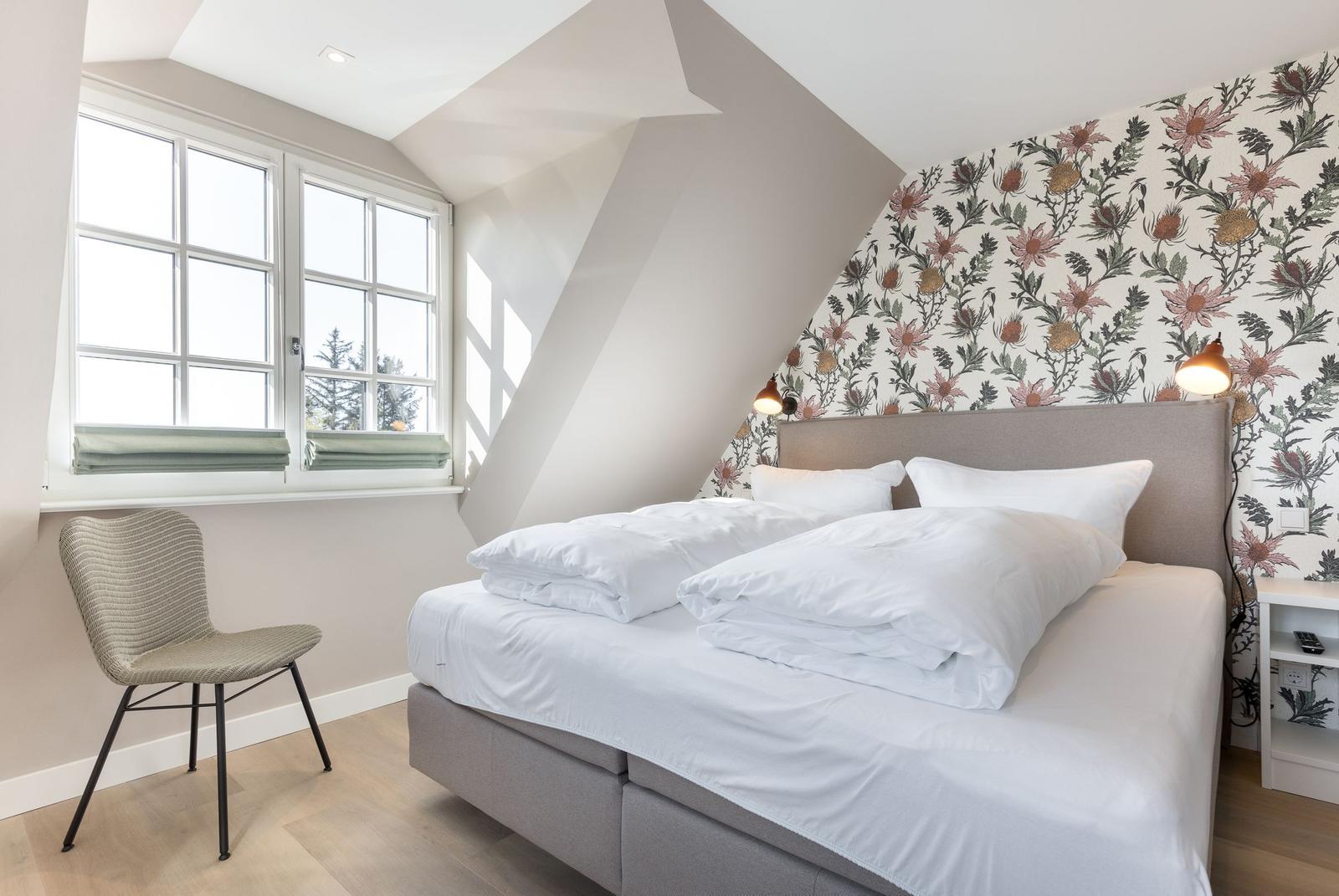 Bedroom with bed, chair, and window. Wall with floral pattern.