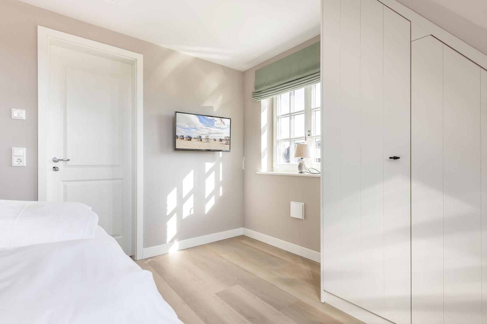 Bedroom with bed, TV, and window with green roller blind.