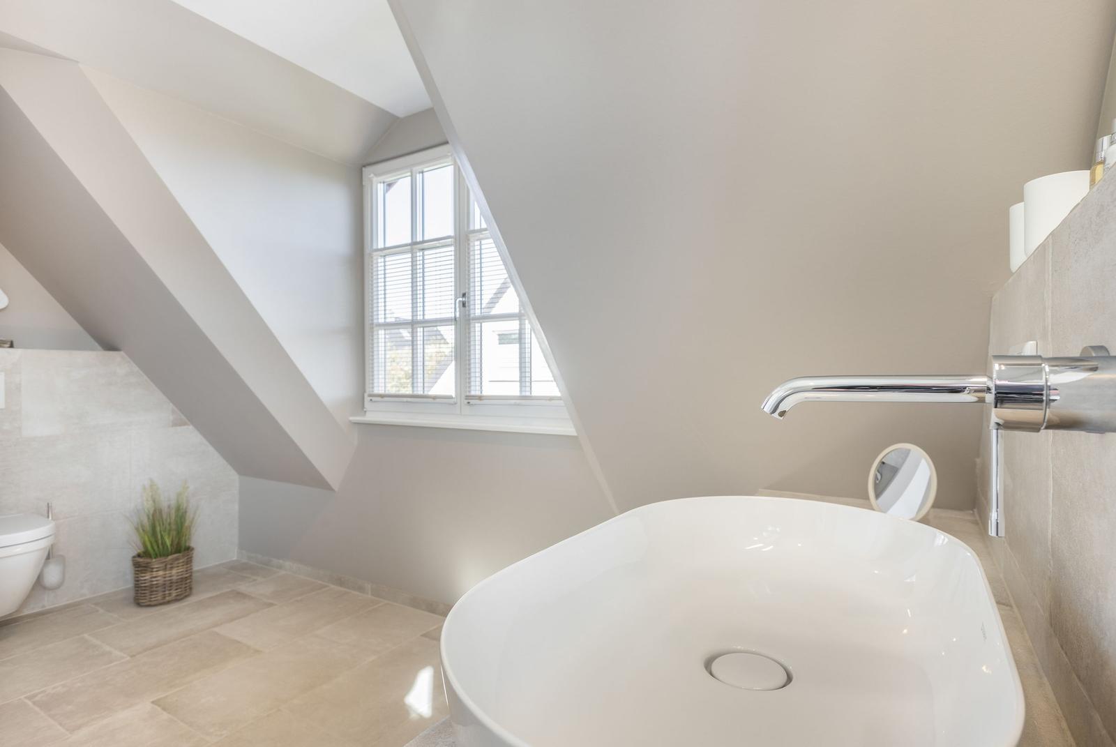 Bathroom with sloped ceilings, window, sink, and toilet.