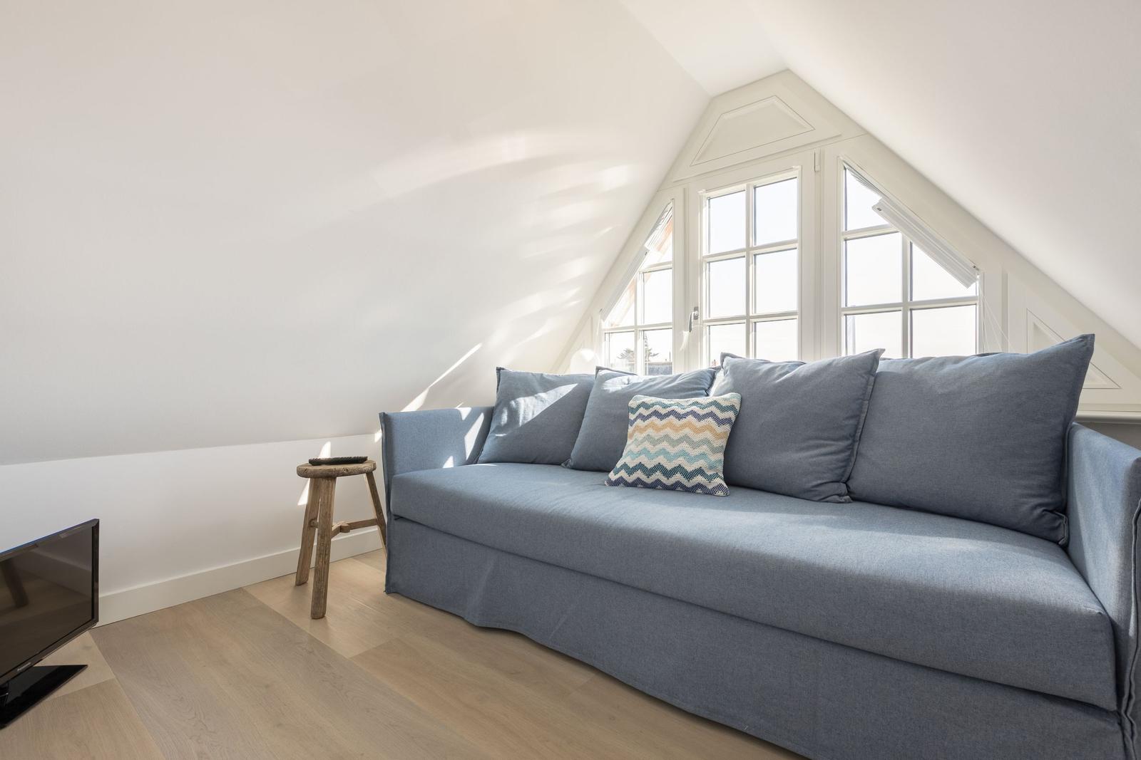 A room with a gray sofa, a wooden stool, and a TV under a skylight window.