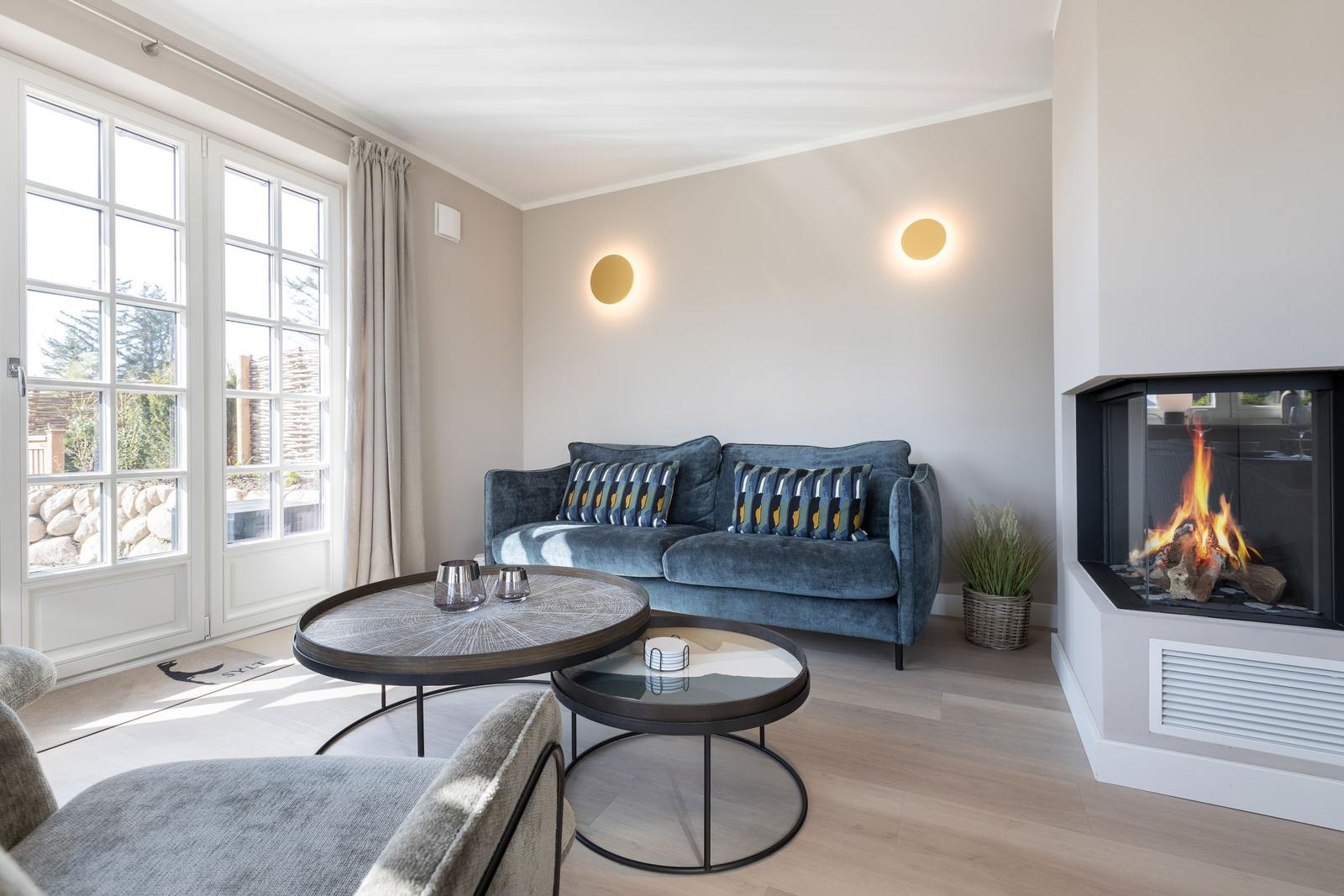 Living room with sofa, fireplace, and tables. Windows to the outside.
