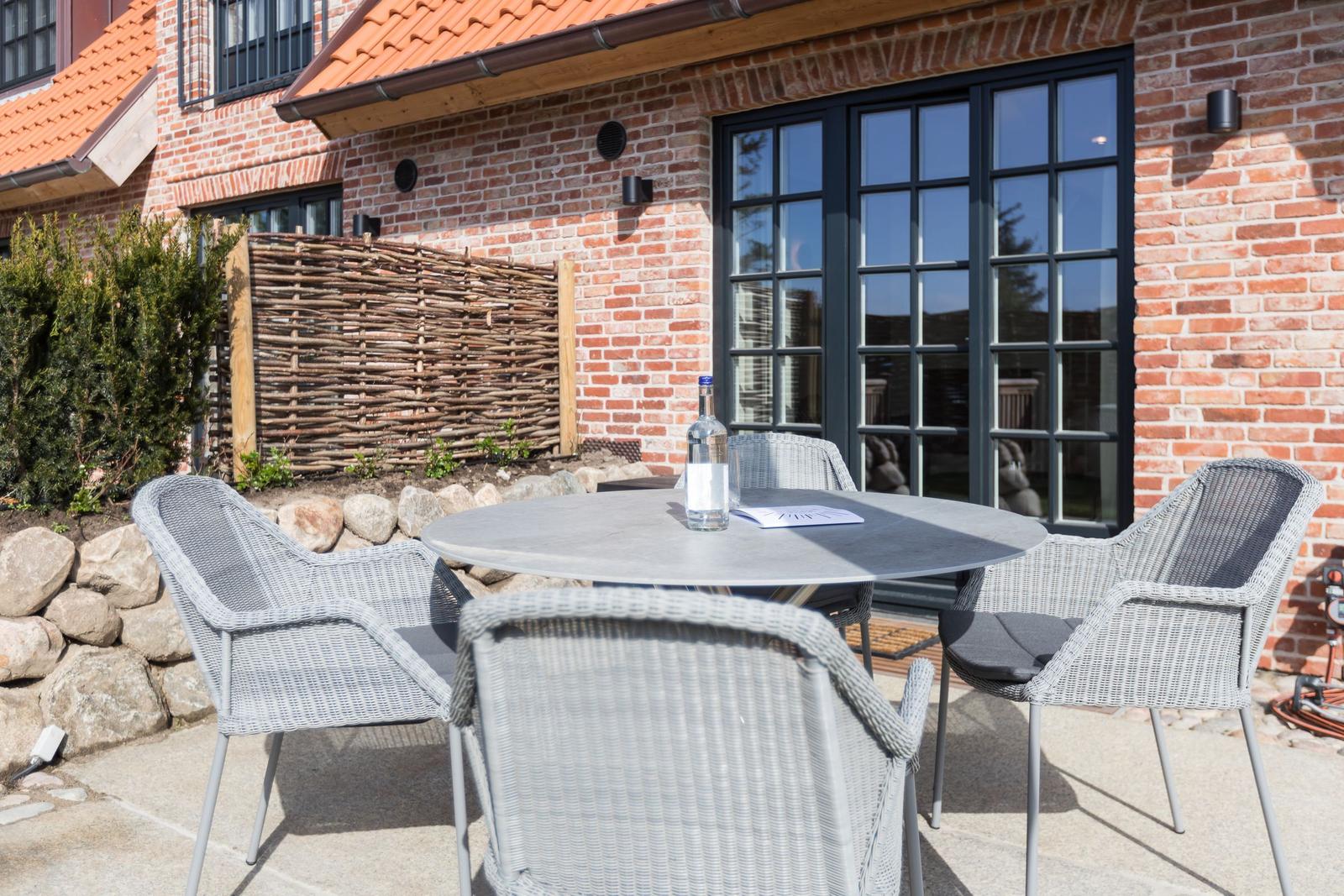 Terrace with round table and four chairs in front of brick house with windows.