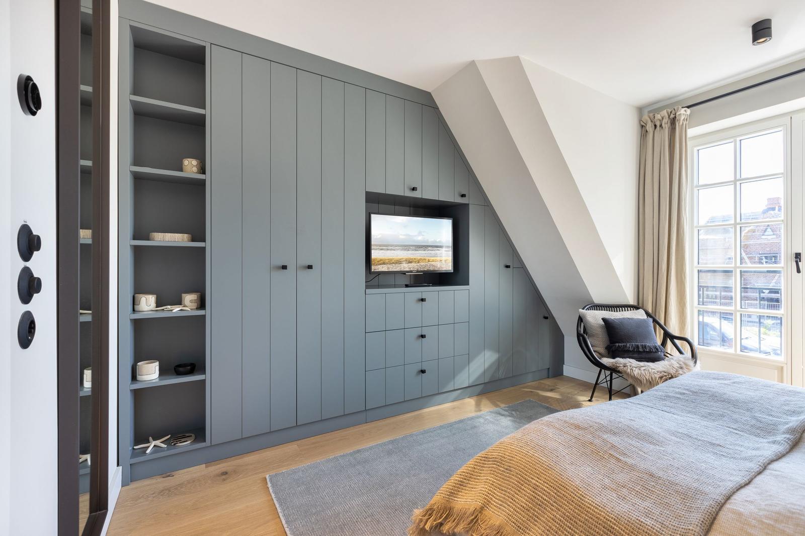 Bedroom with gray closet, TV, and window with view.