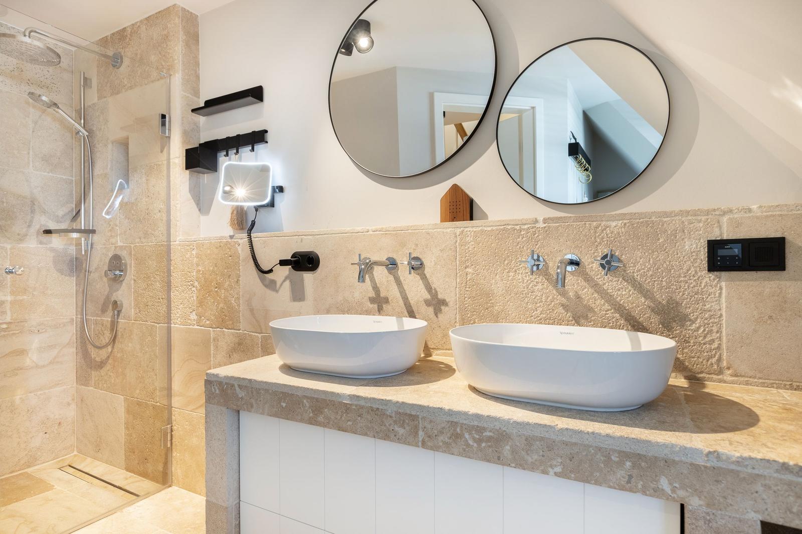 Bathroom with shower, two sinks, and round mirrors on the wall.