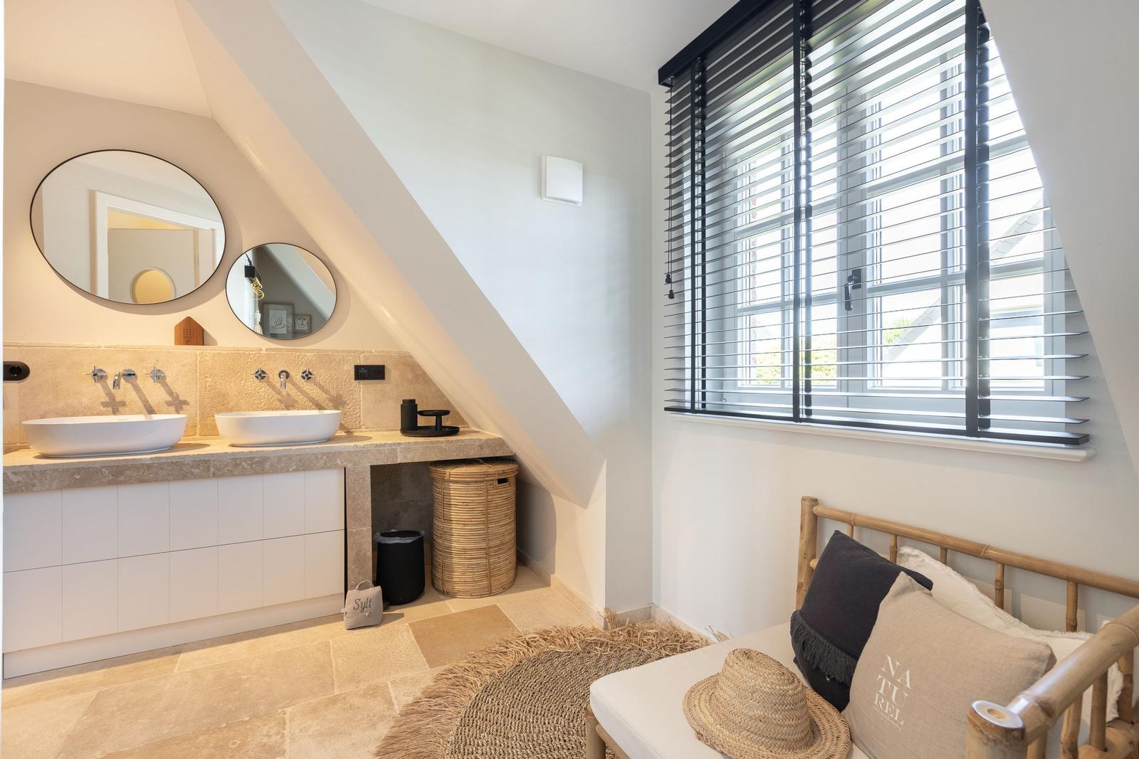 Double sink with mirrors, window with blinds, and seating with cushions.