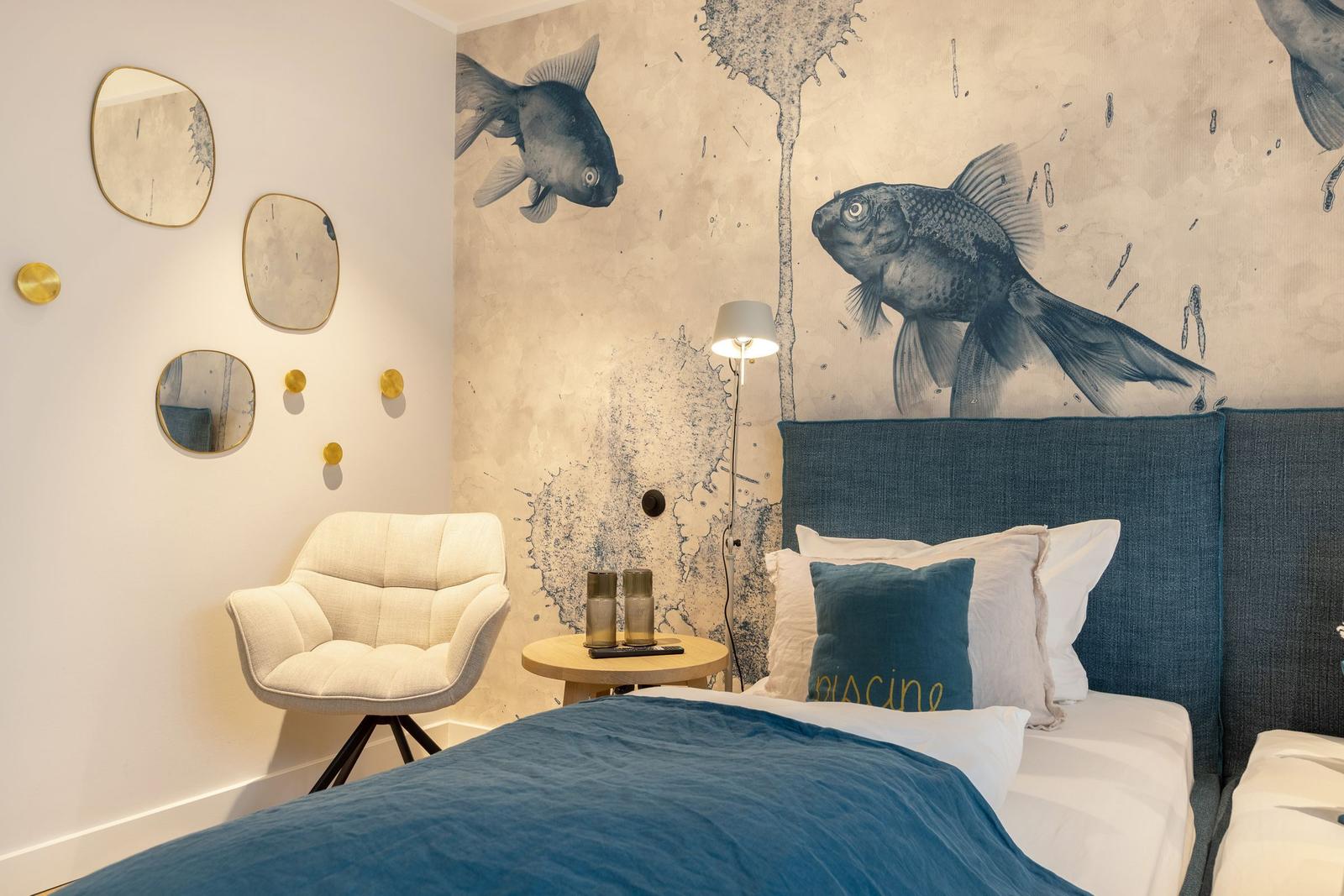 Bedroom with fish-themed wall, blue bed, and white chairs.