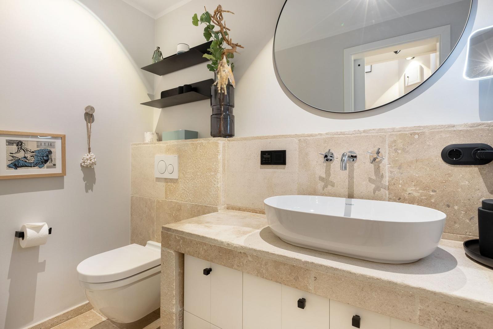 Bathroom with sink, mirror, and toilet. Stone wall and modern faucets.