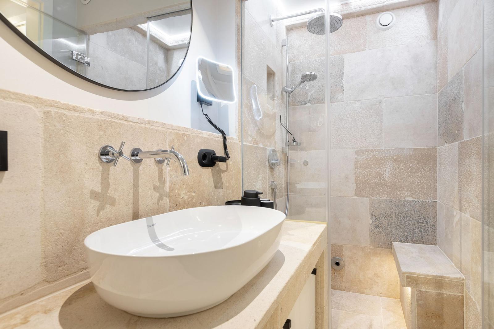 Bathroom with shower, sink, and mirror on stone wall