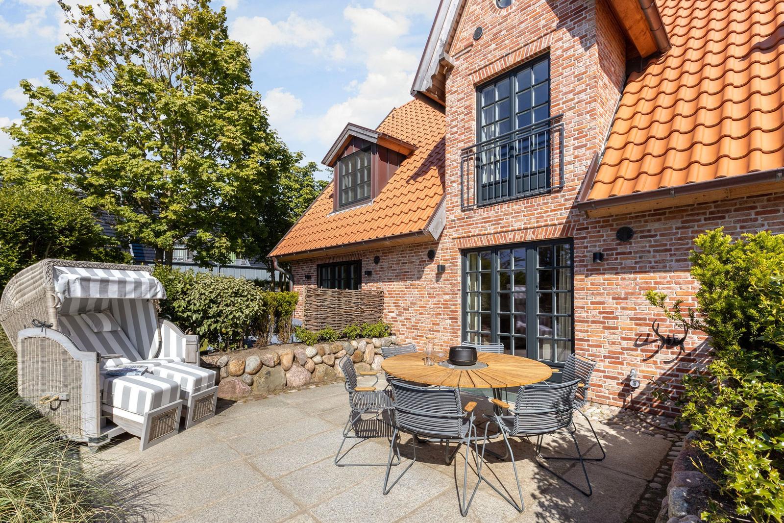 Terrace with garden lounger, table and chairs in front of brick house with dormers.