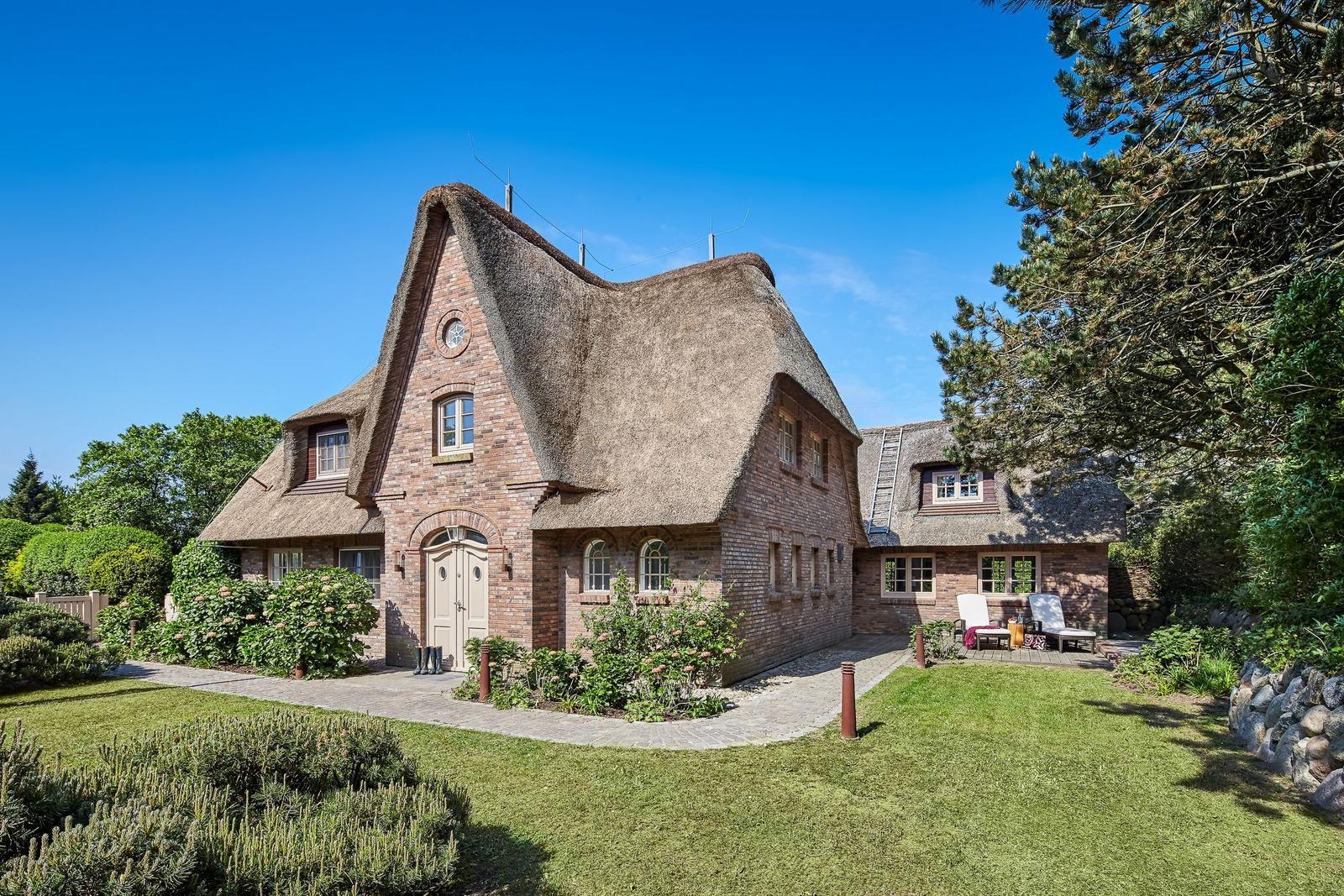 House with thatched roof, garden, and terrace with lounge chairs.