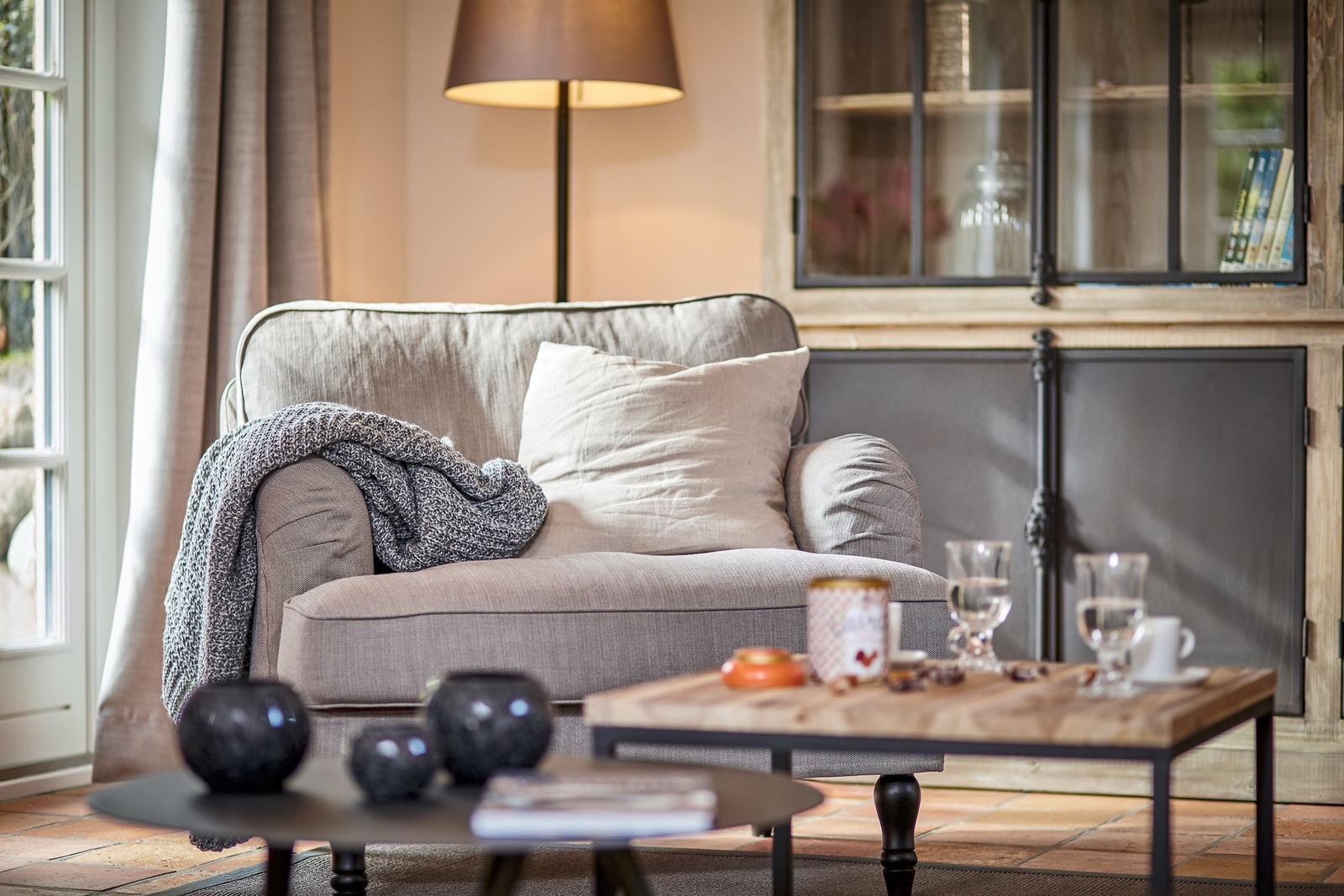 A gray armchair with cushions and a blanket near a window.