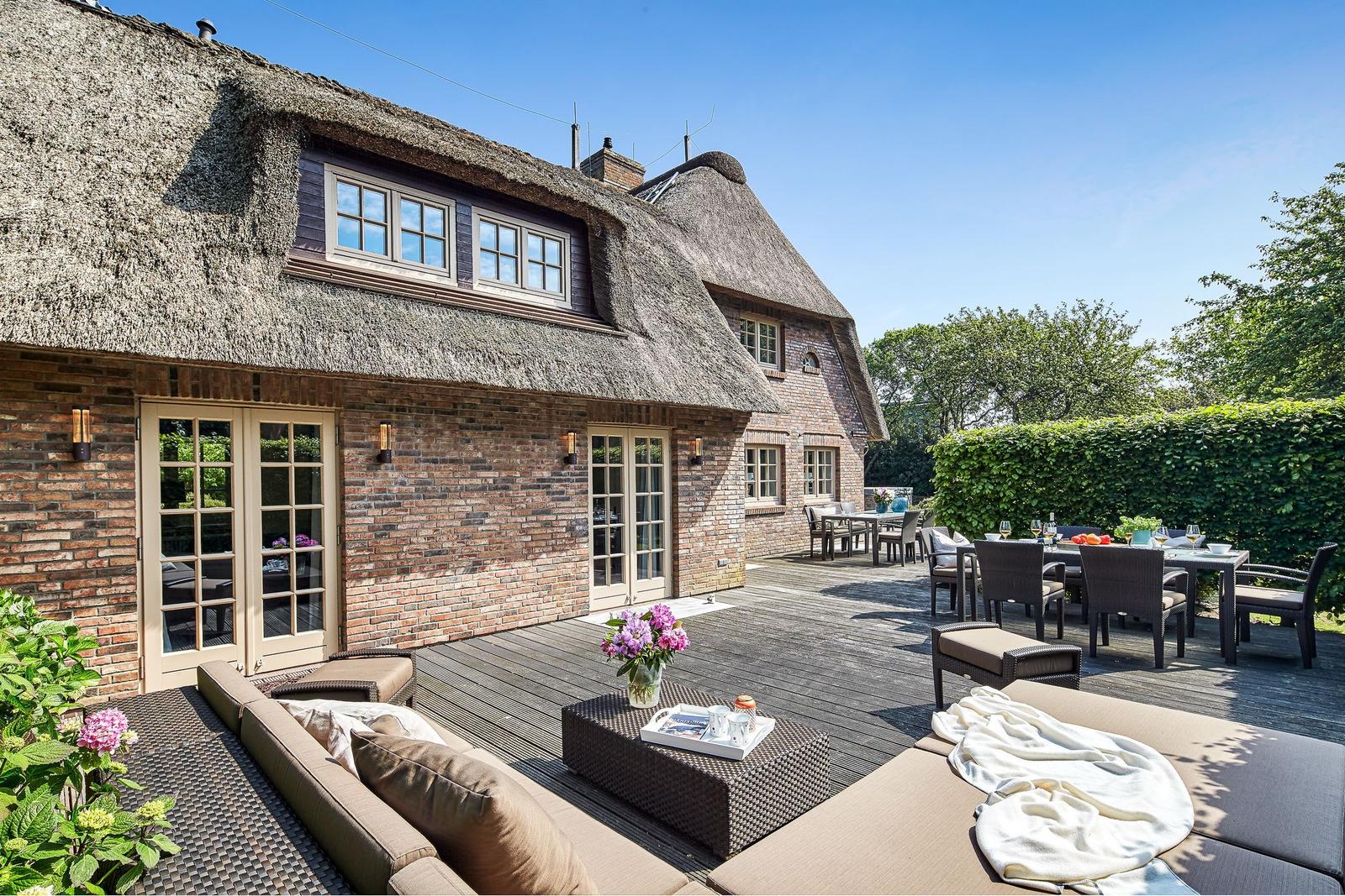 House with thatched roof and terrace with seating and table.