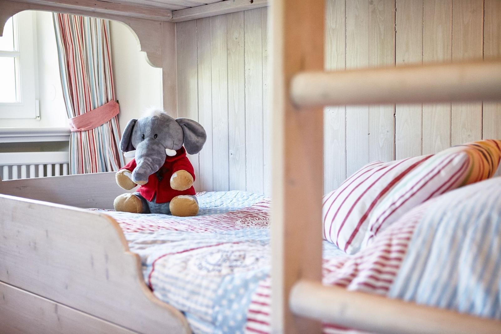 A crib bed with pillows and a stuffed toy. In the background, a window with curtains.