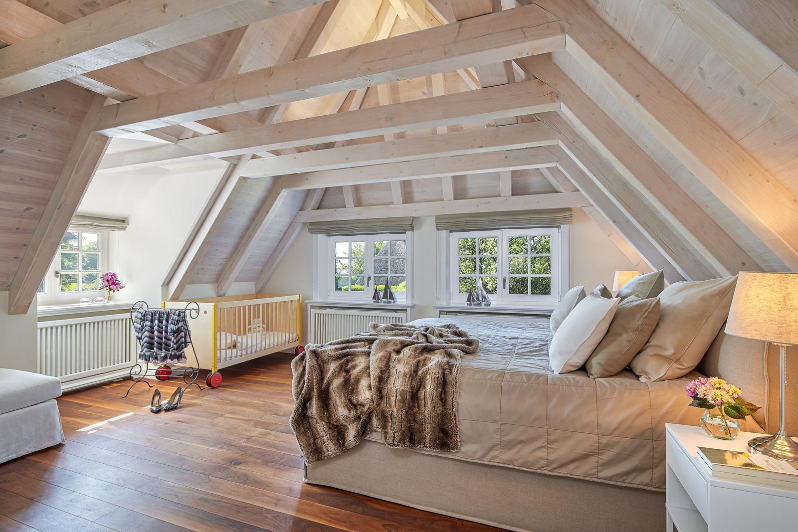 Bedroom with wooden beam ceiling, bed, crib, and windows.