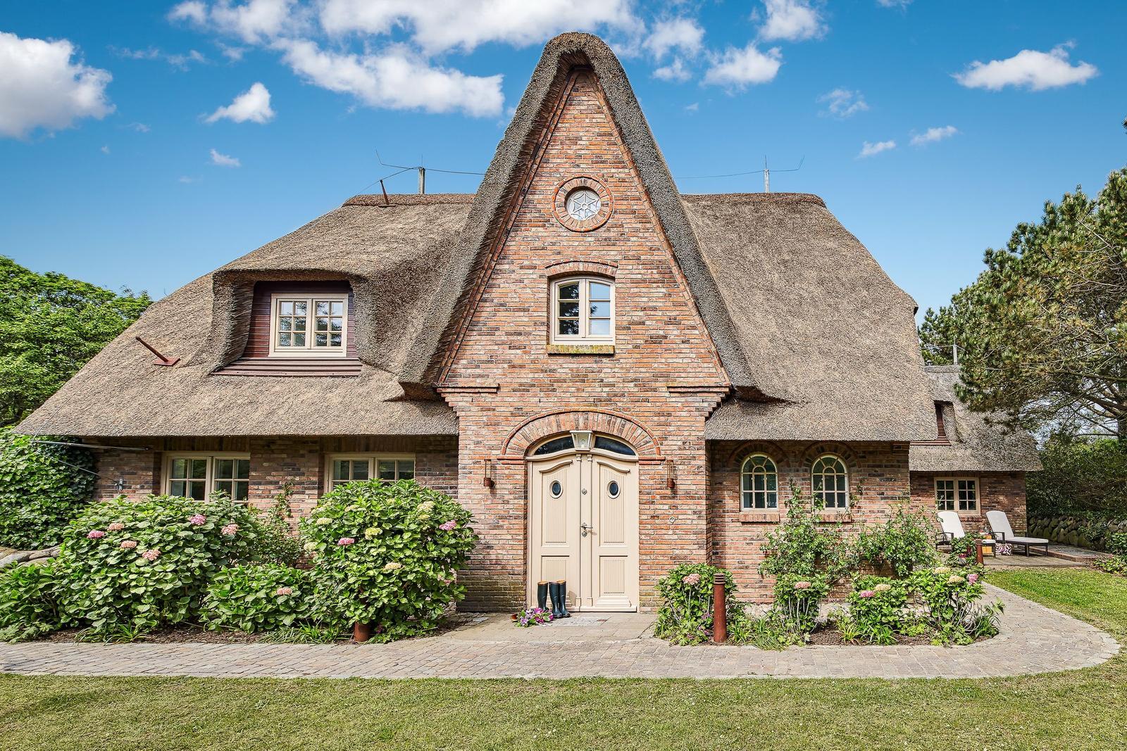 House with thatched roof, brick facade, and paved driveway with flower beds.