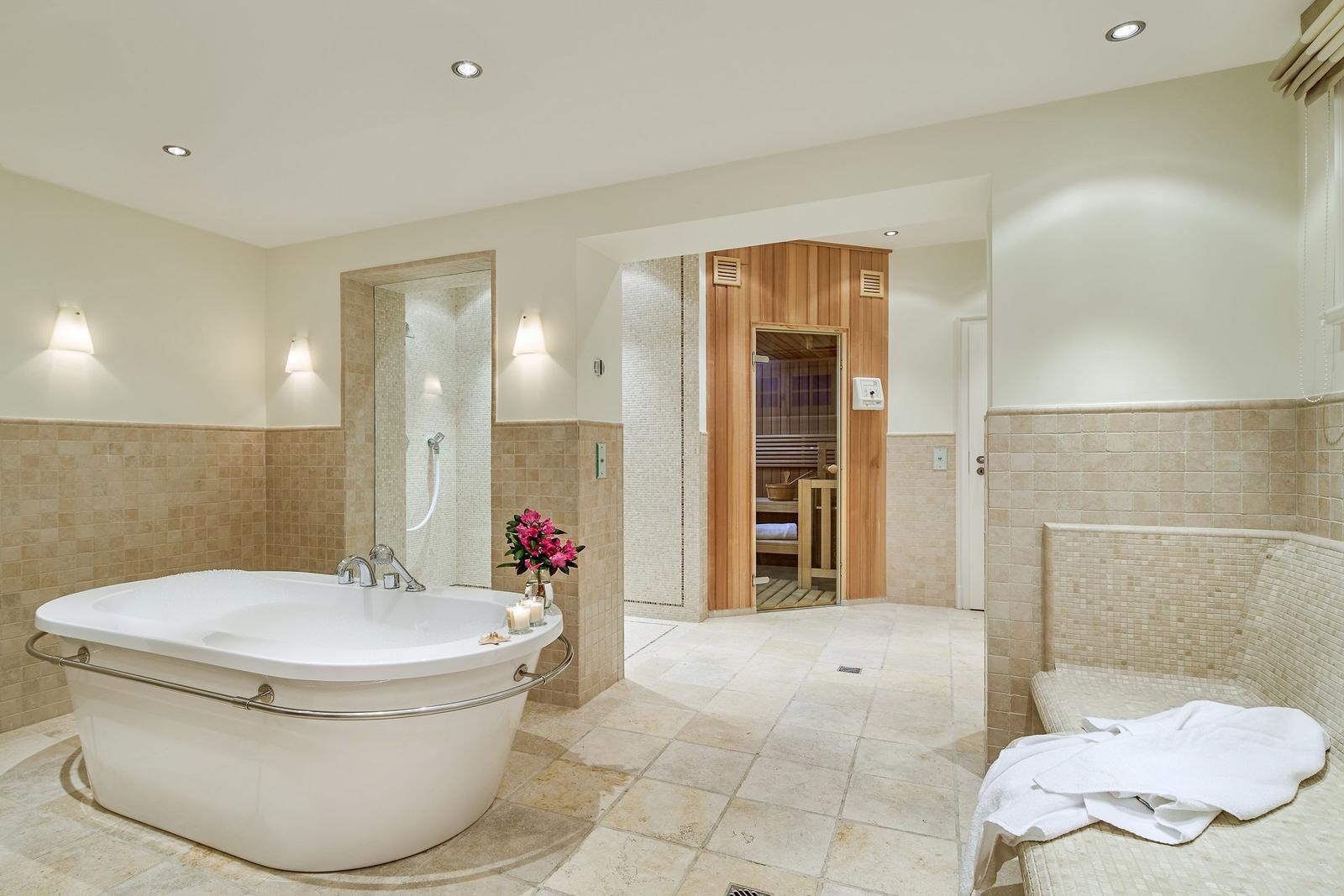 Bath with whirlpool, shower, and sauna. White bathtub, wooden sauna, and mosaic tiles.